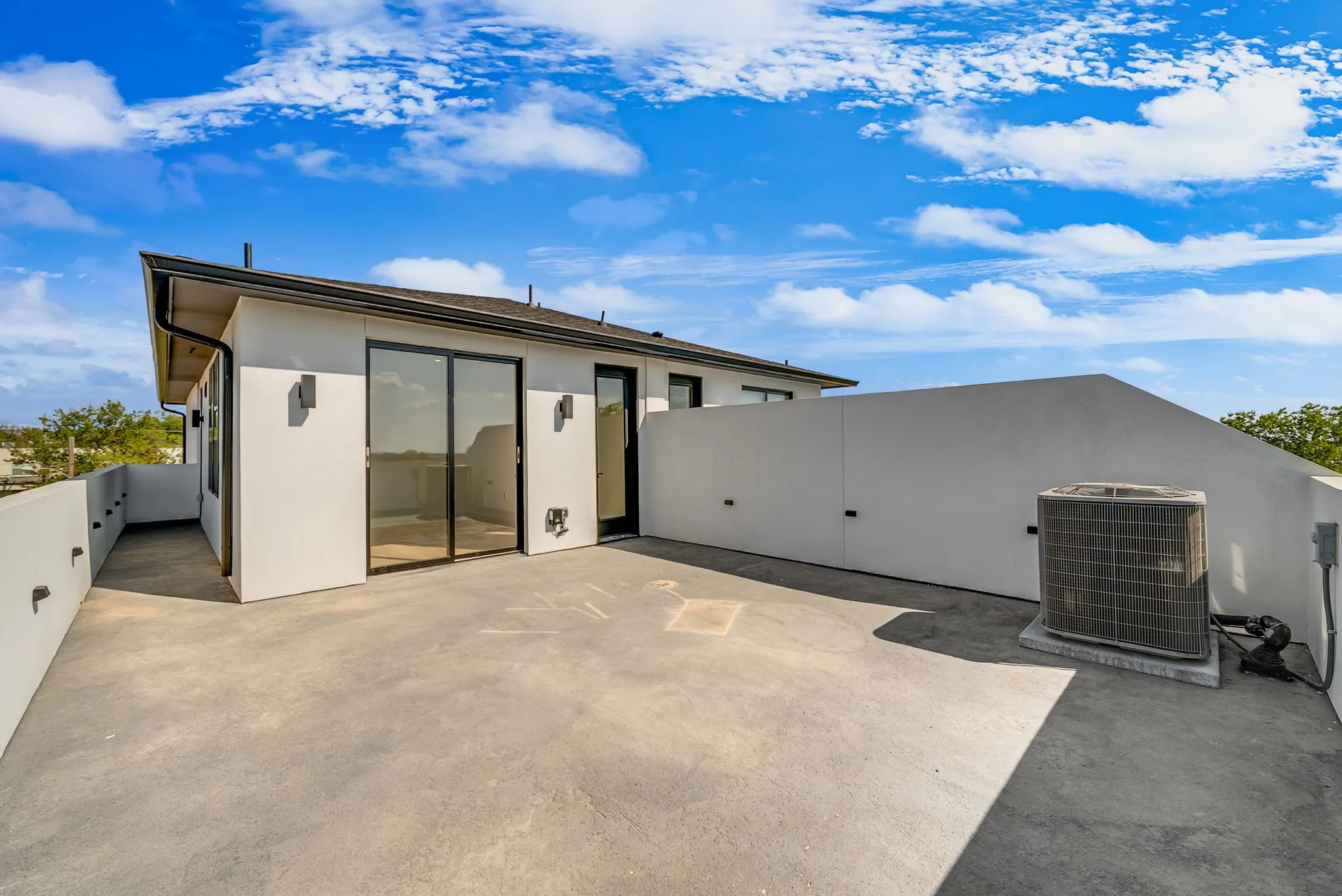 Rooftop patio with concrete flooring, stucco exterior, black-framed sliding glass doors, and modern exterior sconces