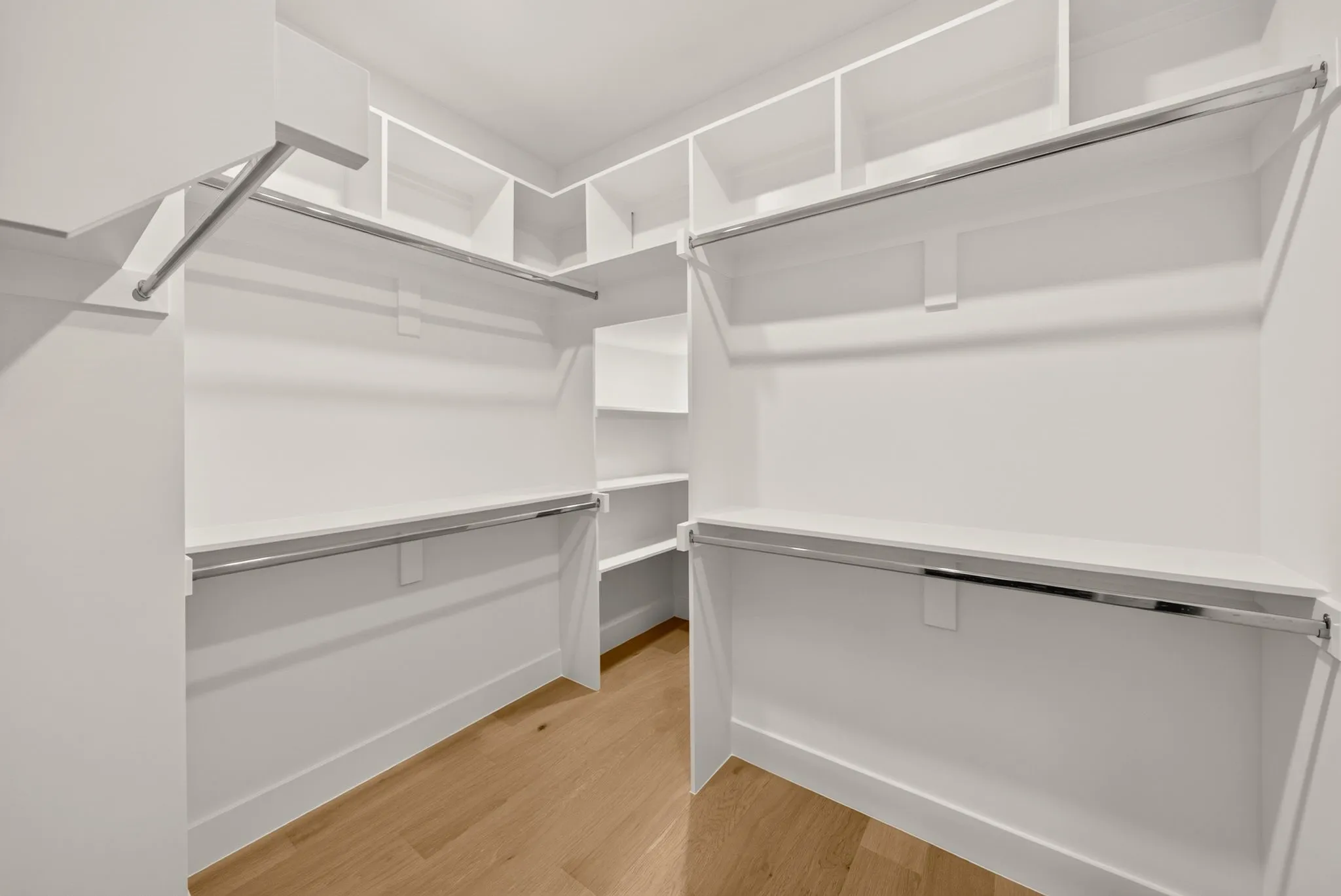 Walk-in closet featuring built-in white shelving, multiple hanging rods, and wood-finish flooring