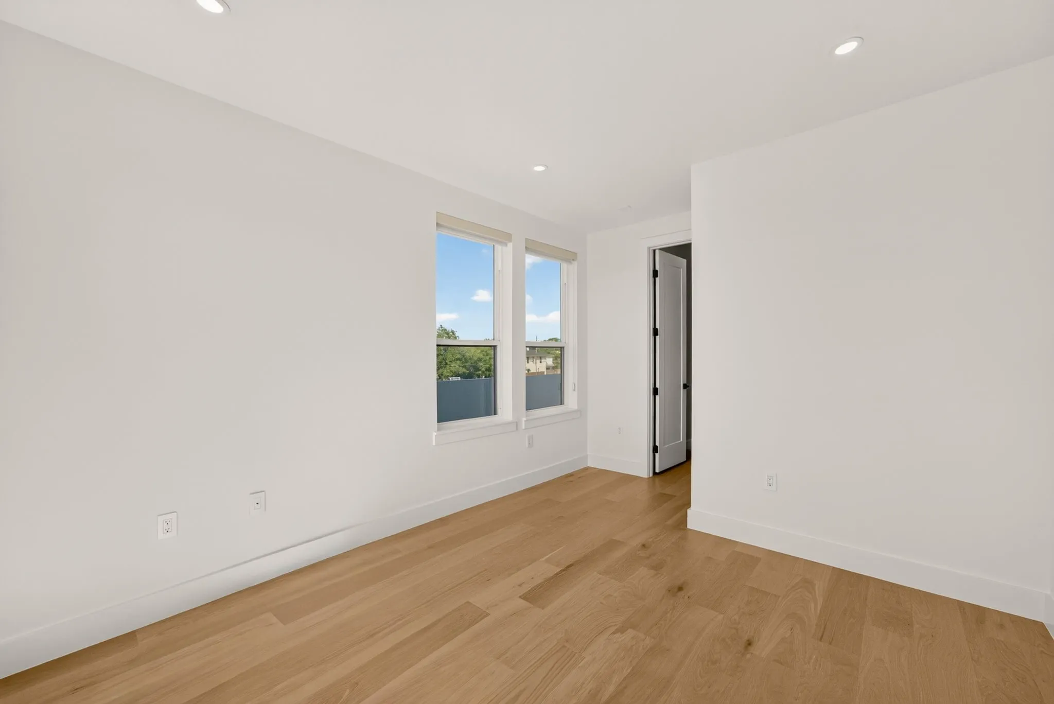 Bright corner bedroom showcasing gleaming wood-finish flooring, white walls, and abundant natural light from dual glass doors with scenic outlooks