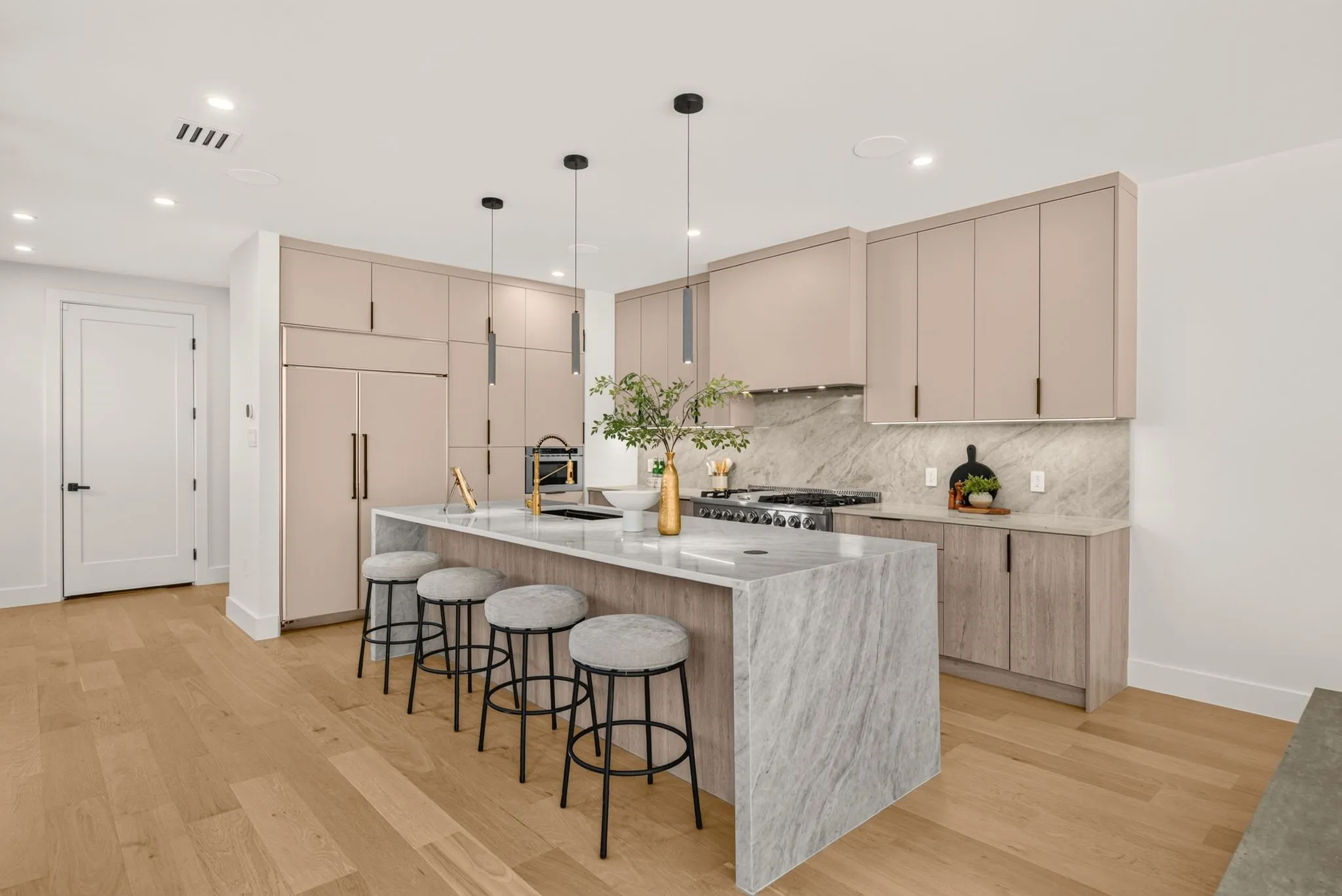 Modern kitchen featuring light wood-finish flooring, a waterfall island with a stone countertop, integrated refrigerator, and sleek flat-panel cabinetry