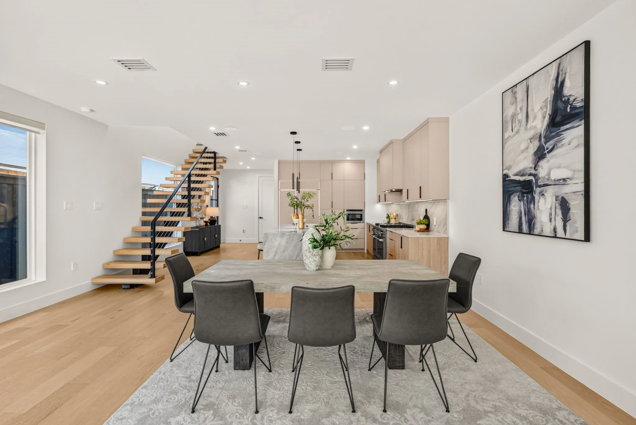 Open-concept living space with light wood-finish flooring, recessed lighting, and a modern floating staircase with black railings