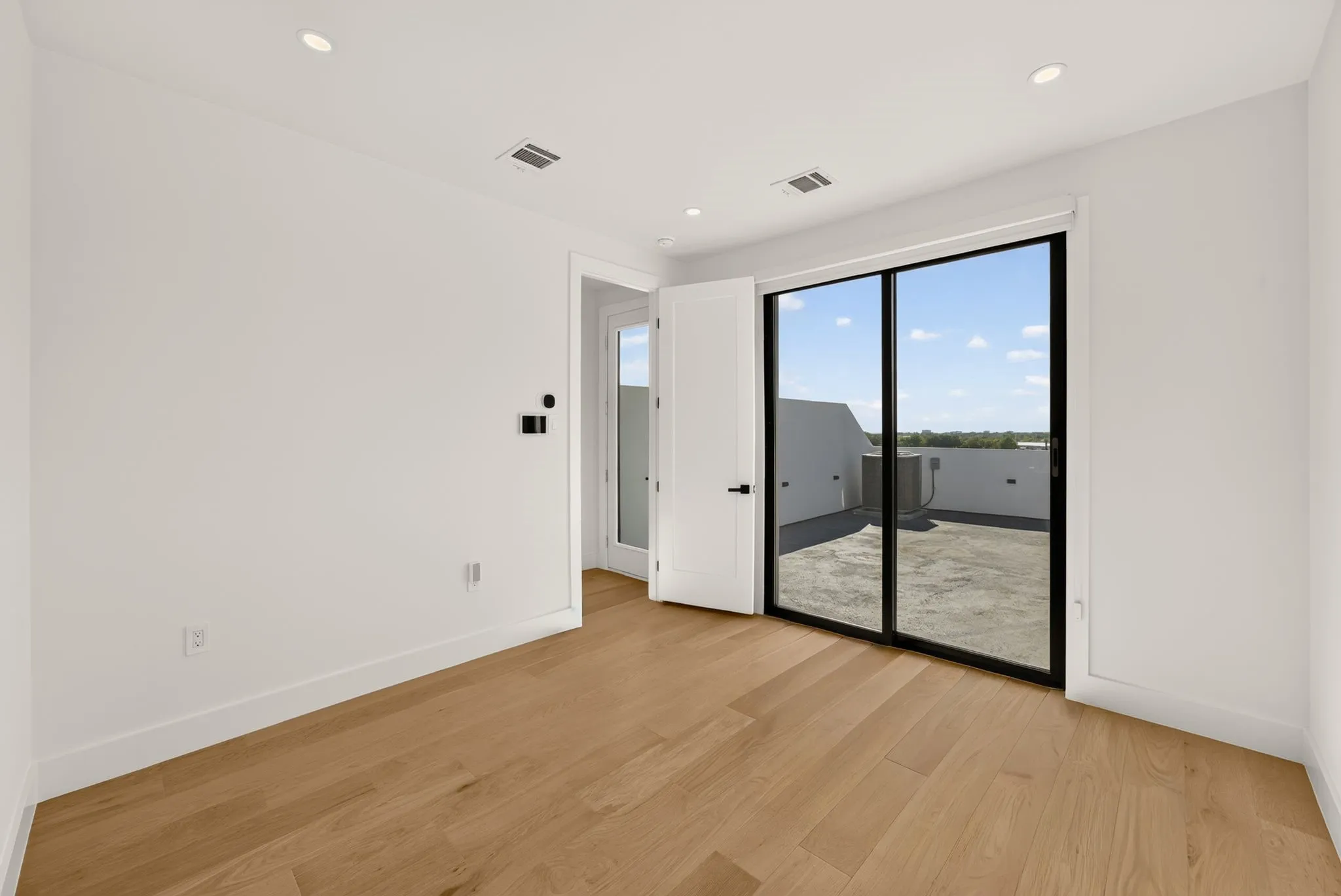 Light wood-finish flooring, recessed ceiling lighting, white walls, and a large sliding glass door