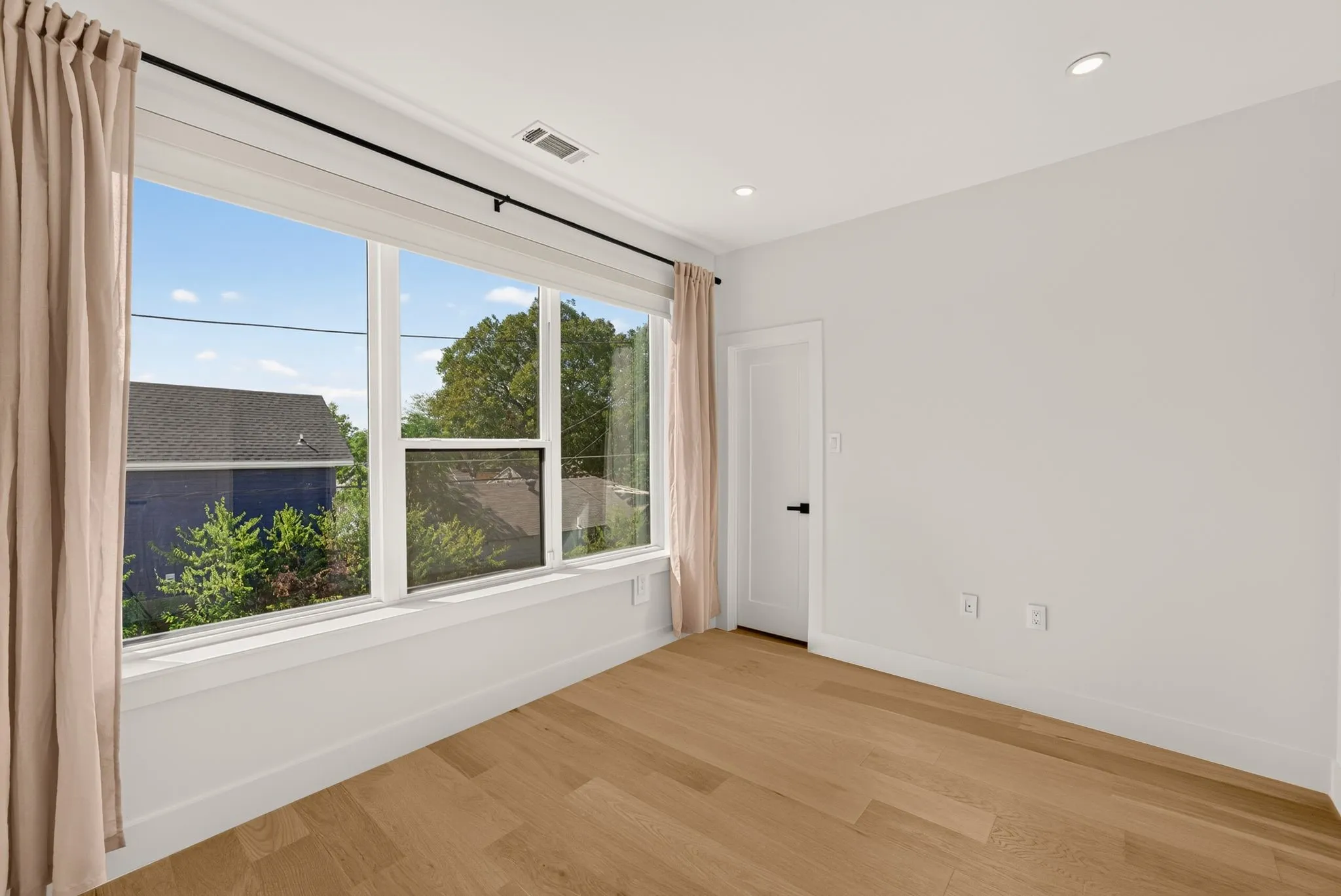 Hardwood-style flooring, expansive windows, recessed lighting, and a white paneled door with matte black hardware