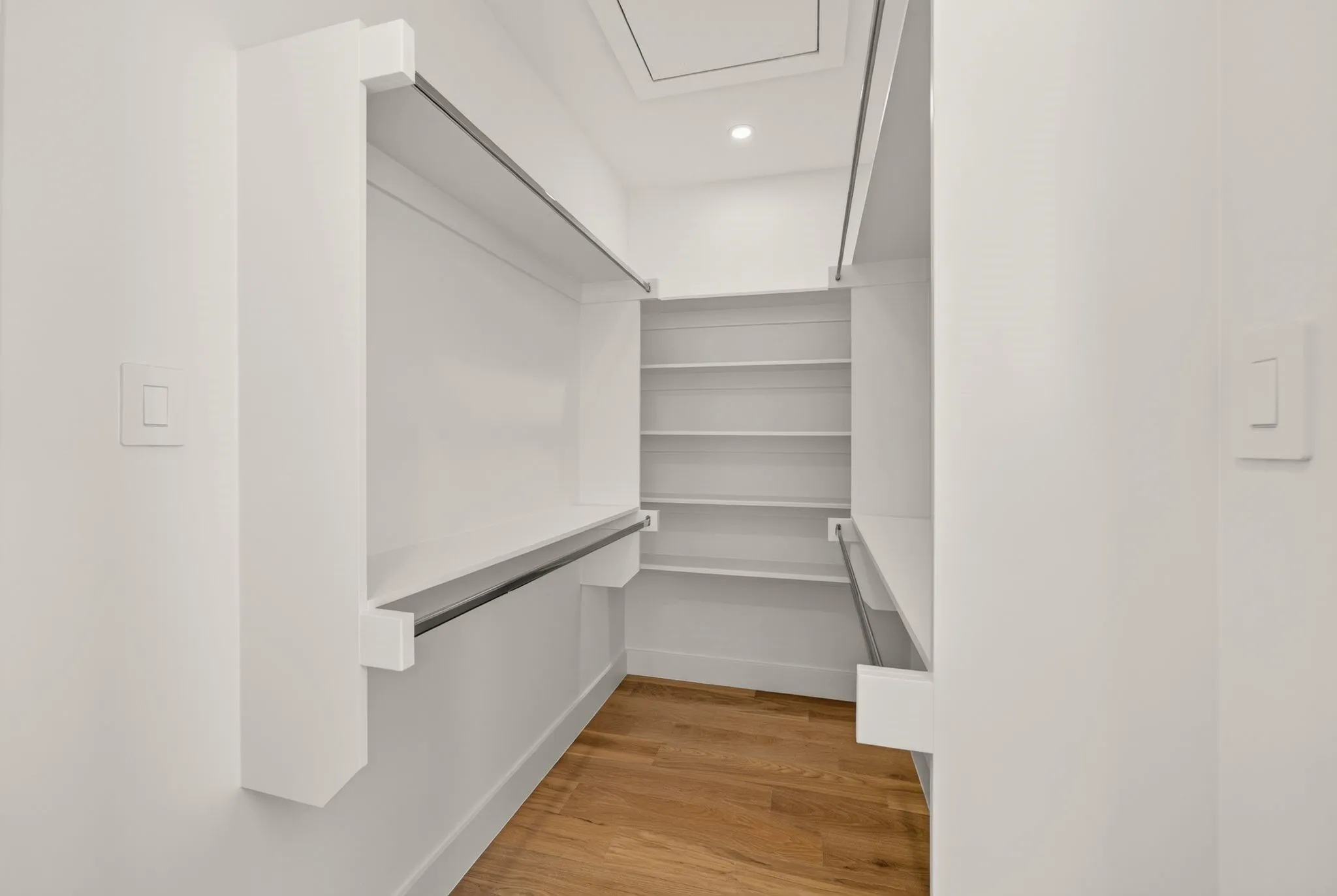 Walk-in closet with wood-finish flooring, built-in shelving, two hanging rods, and recessed lighting