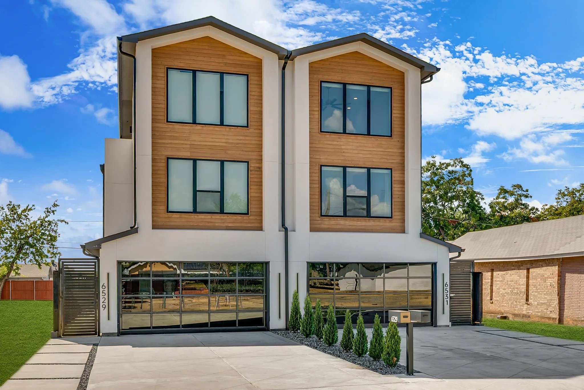 Contemporary exterior with wood-finish siding accents, multiple large windows, and full-glass garage doors