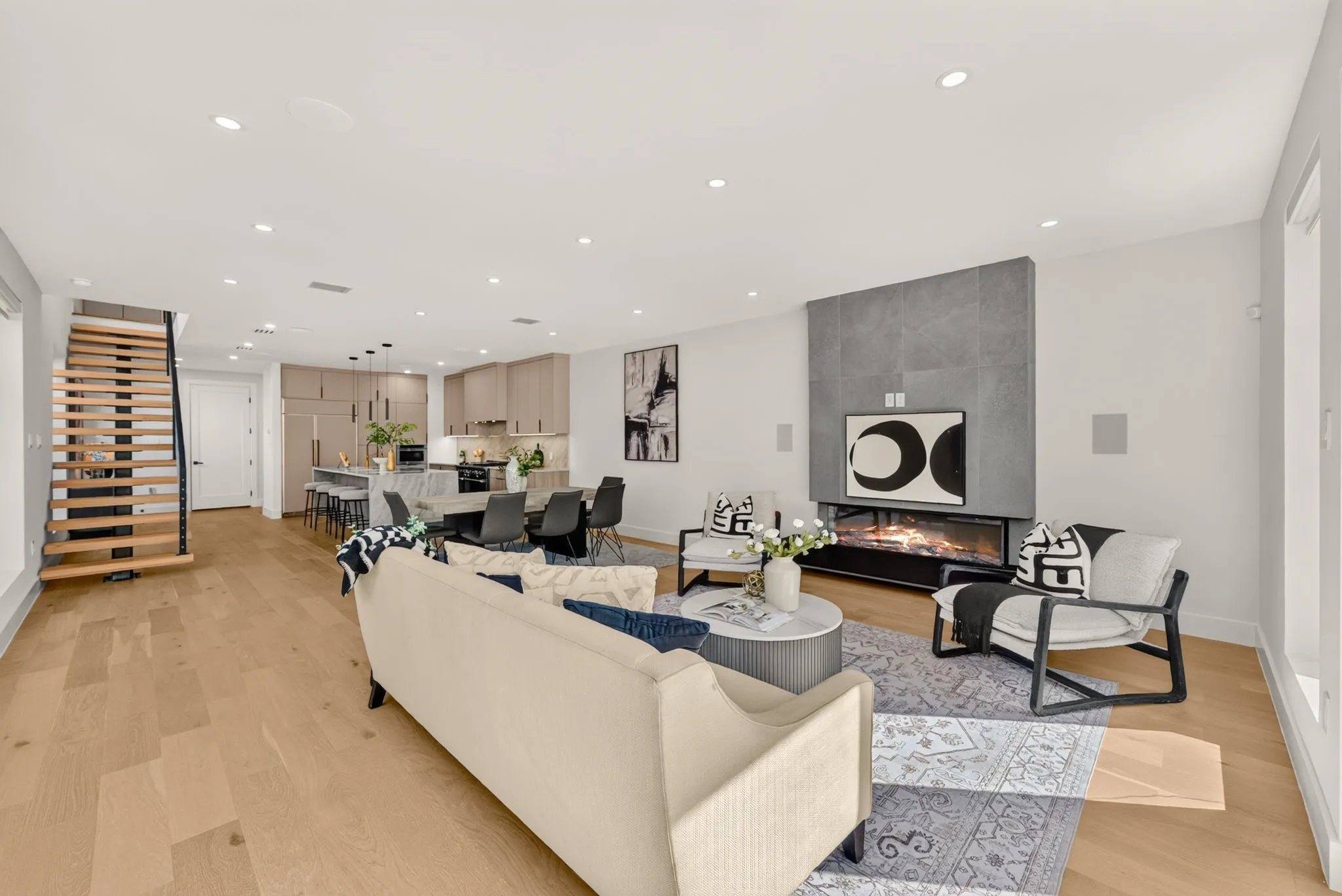 Spacious open-concept living area featuring wood-finish flooring, a modern fireplace with a tiled surround, and recessed lighting