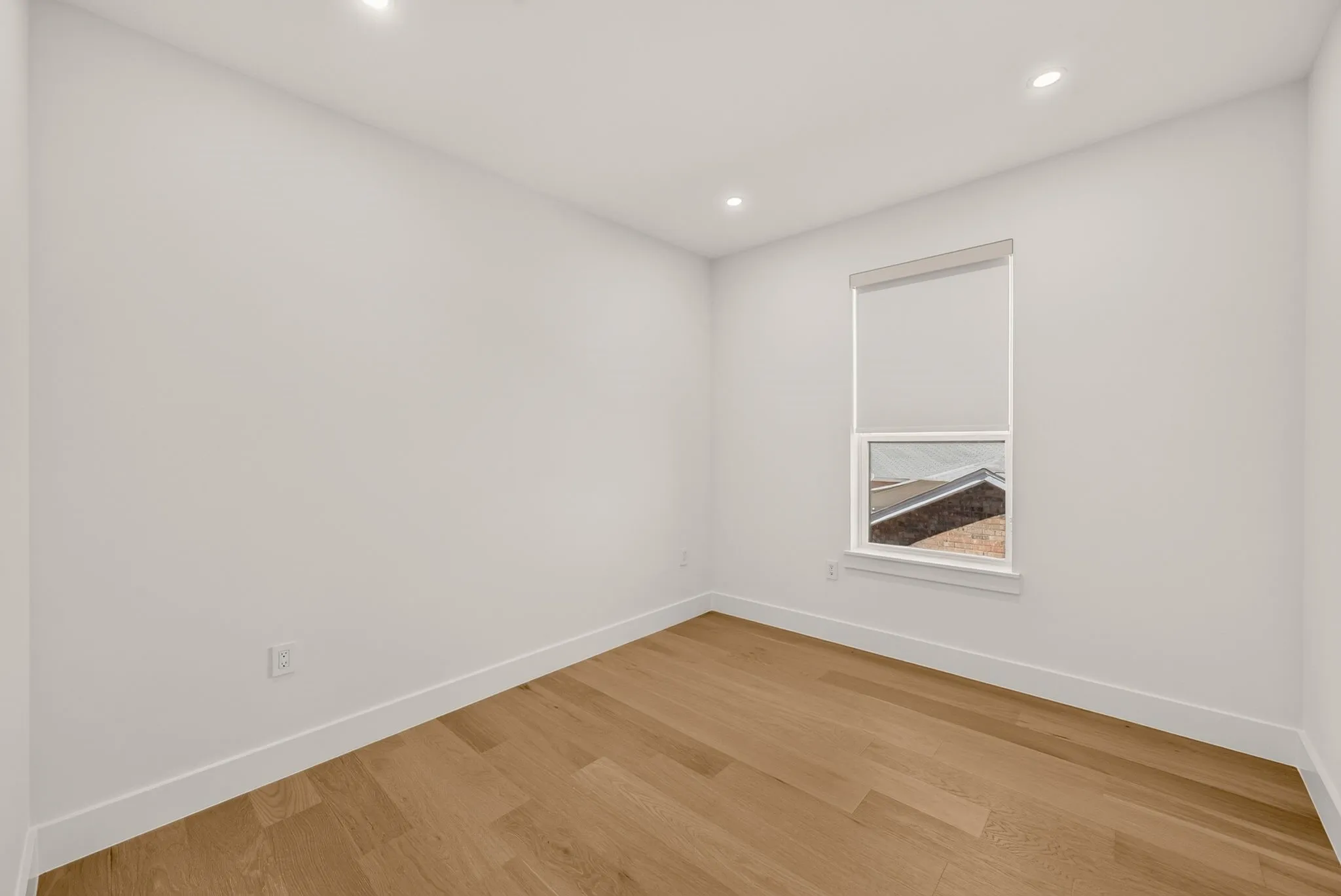 Recessed lighting, light wood-finish flooring, white walls, single window with roller shade, and white trim