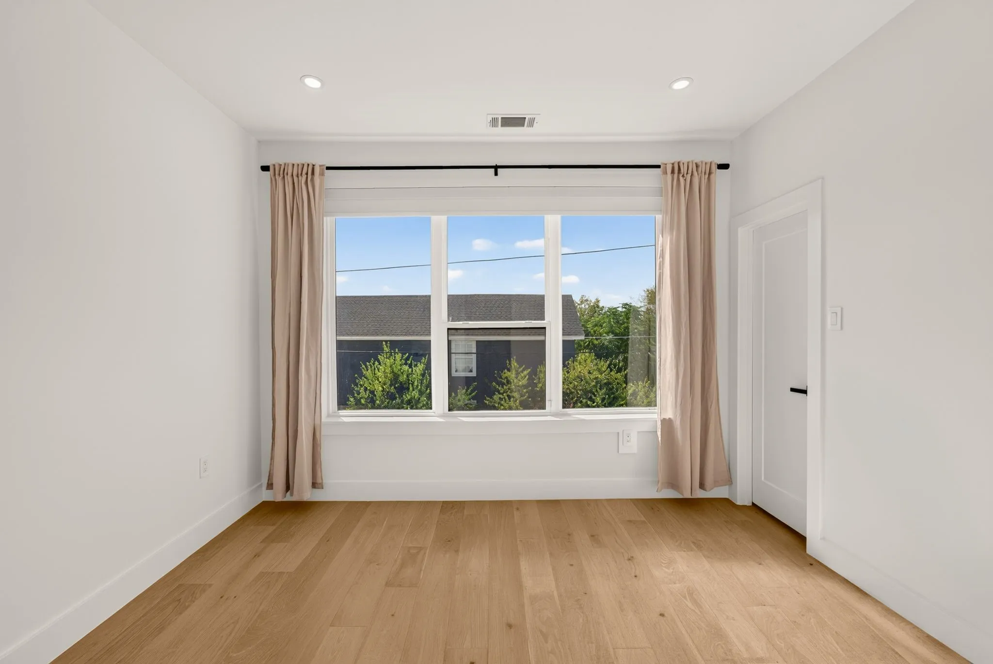 Recessed lighting, wood-finish flooring, white walls, large window, and a white door with black hardware