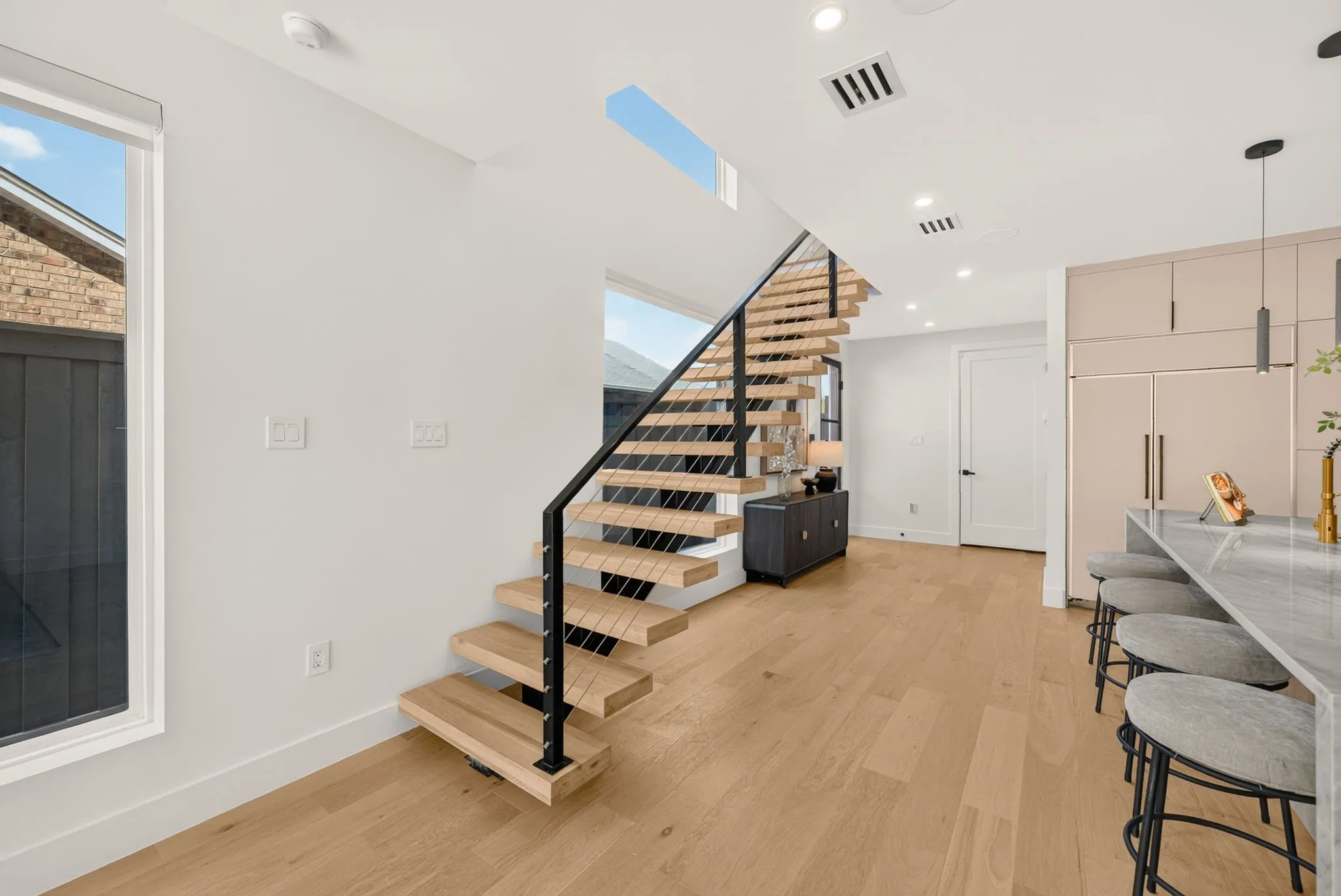 Floating wood staircase with cable railing, wood-finish flooring, recessed lighting, skylight, and integrated kitchen appliances