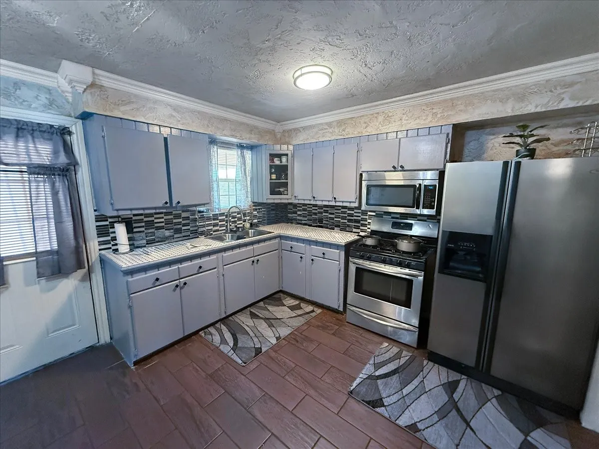 Kitchen featuring sleek dark countertops, grey cabinetry, stainless steel appliances, and tile backsplash.