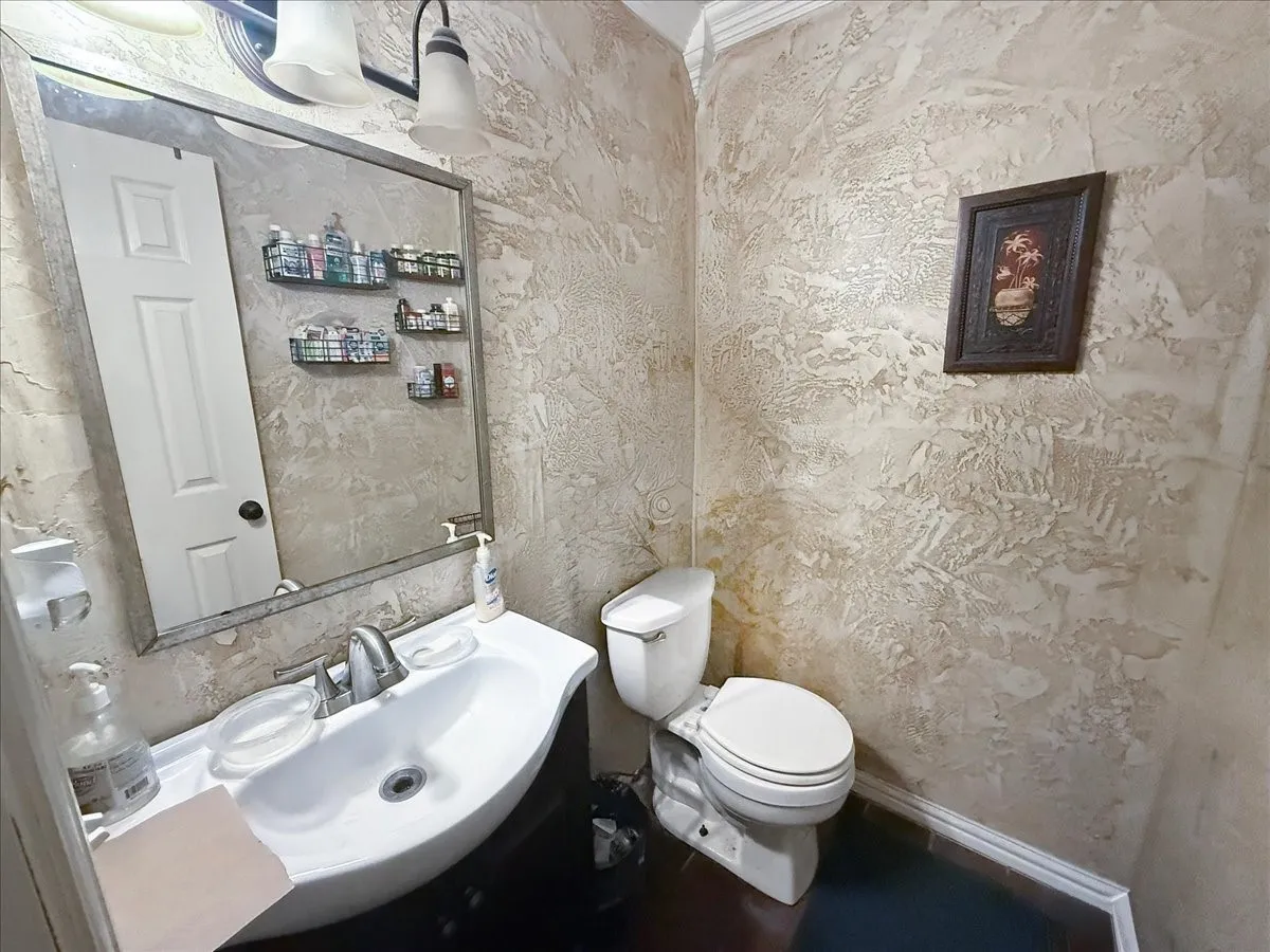 Powder room / bathroom corner featuring pedestal sink, toilet, and textured wall treatment.