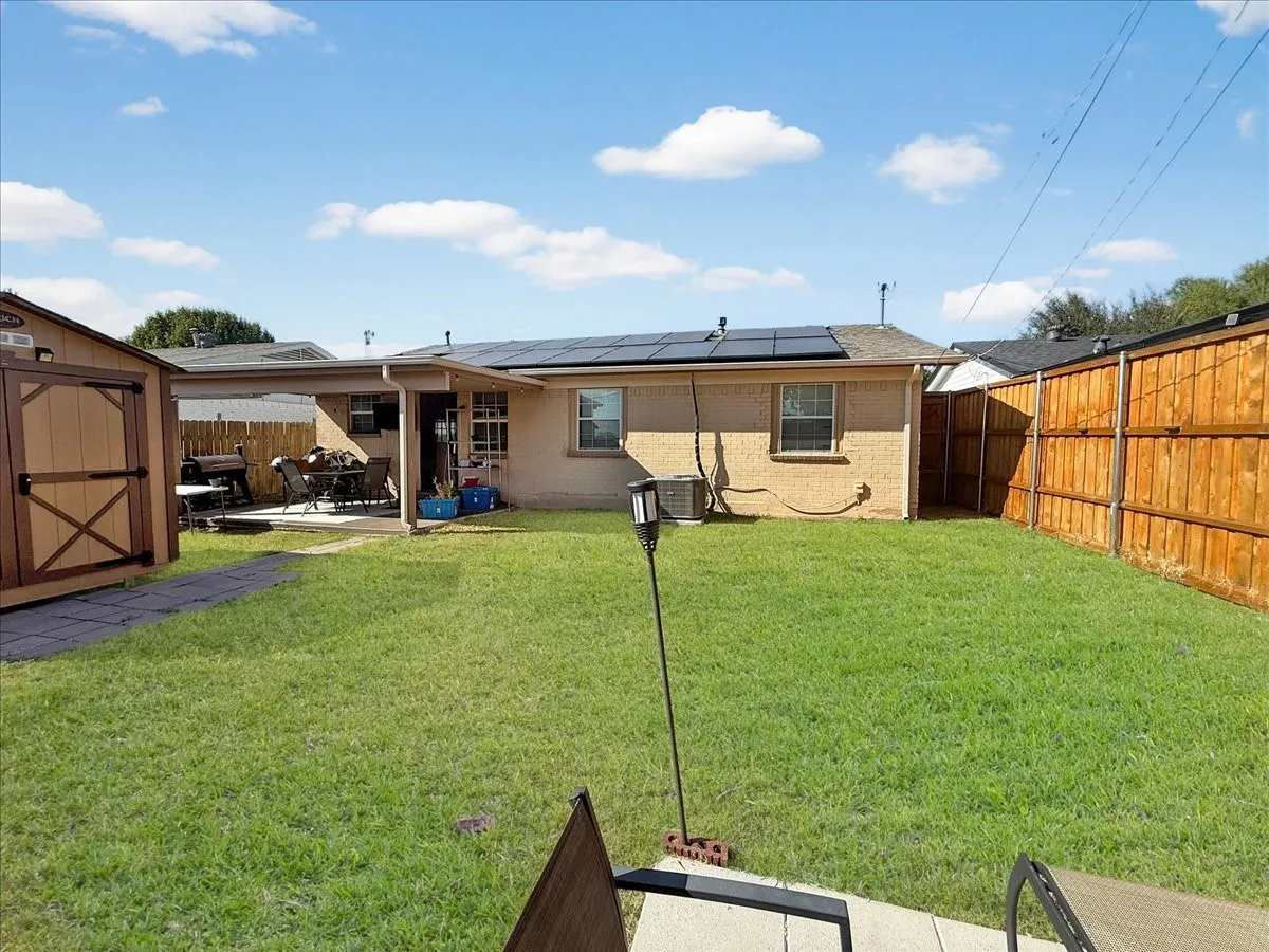 Alternate backyard view displaying open lawn space, perimeter wood fencing, and blue skies.