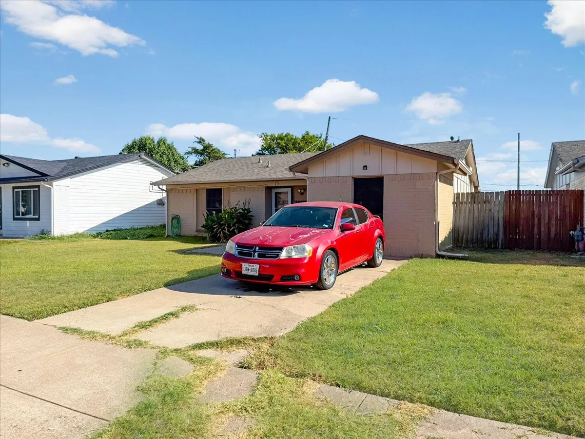 Front exterior view featuring a single-story elevation, paved concrete driveway, mature shade tree, and green lawn.