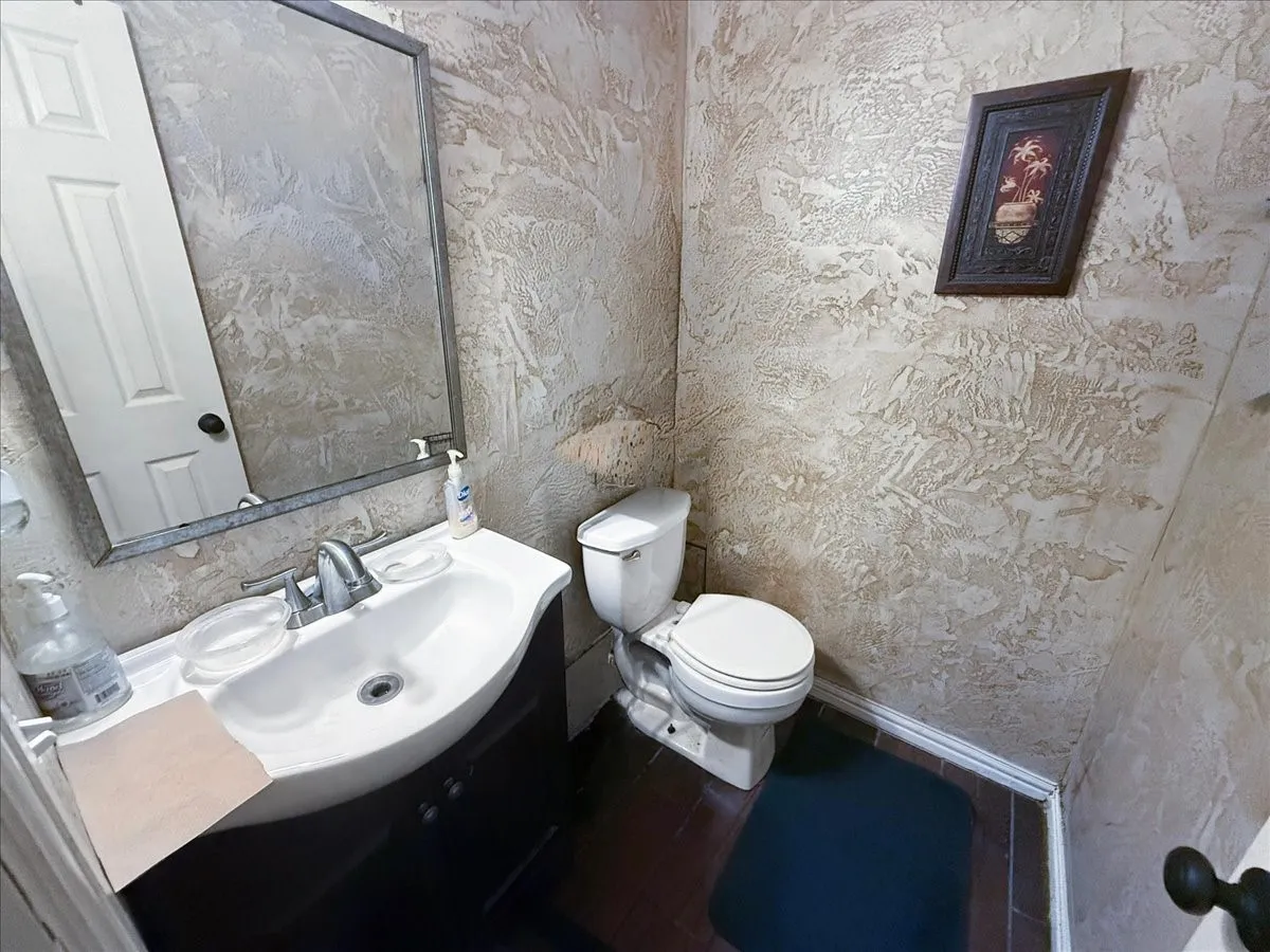 Full bath view displaying white vanity sink, toilet, and dark tile floor accents.