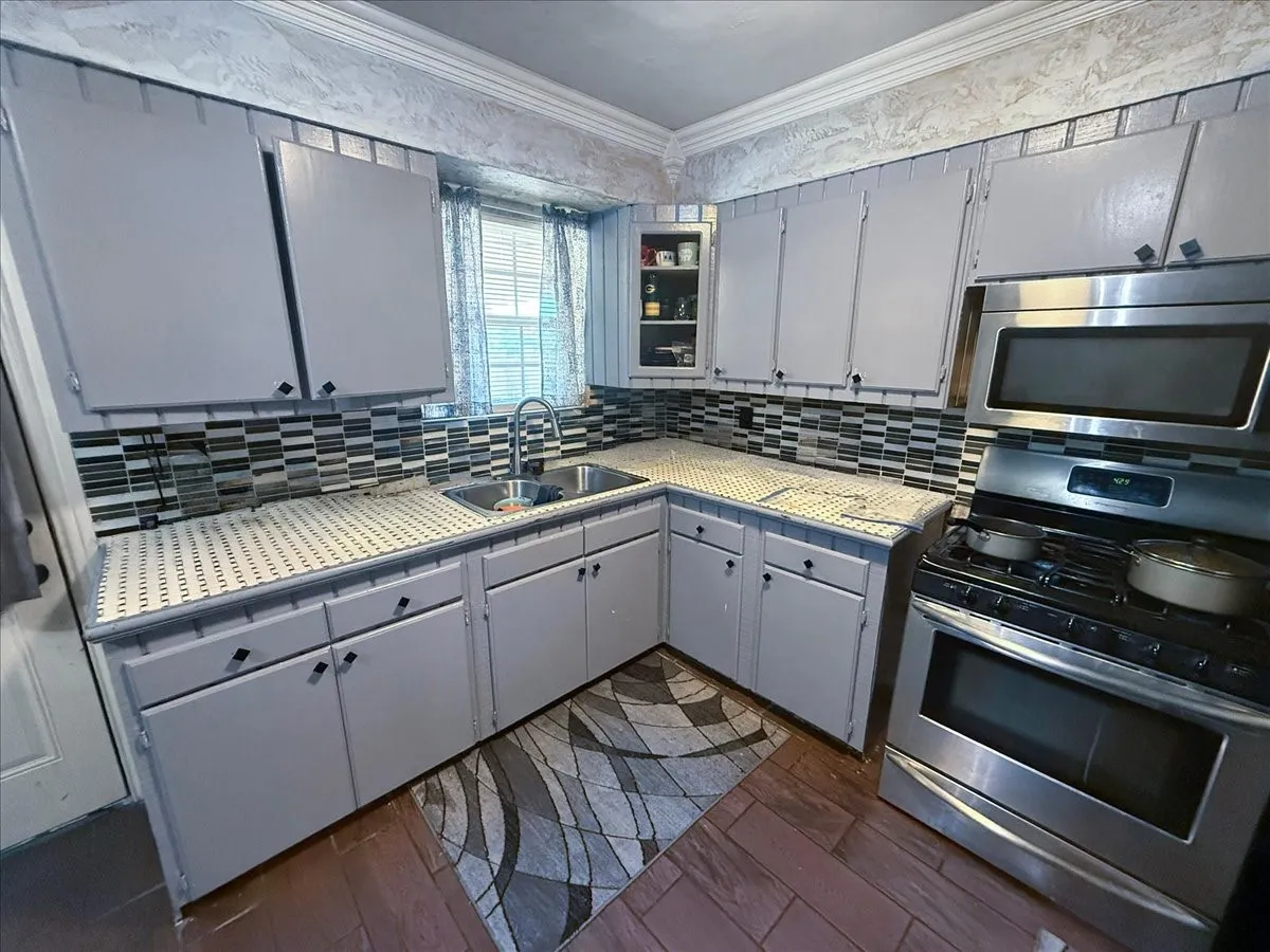 Kitchen detail view featuring double sink set under window light, subway tile backsplash, and microwave hood.