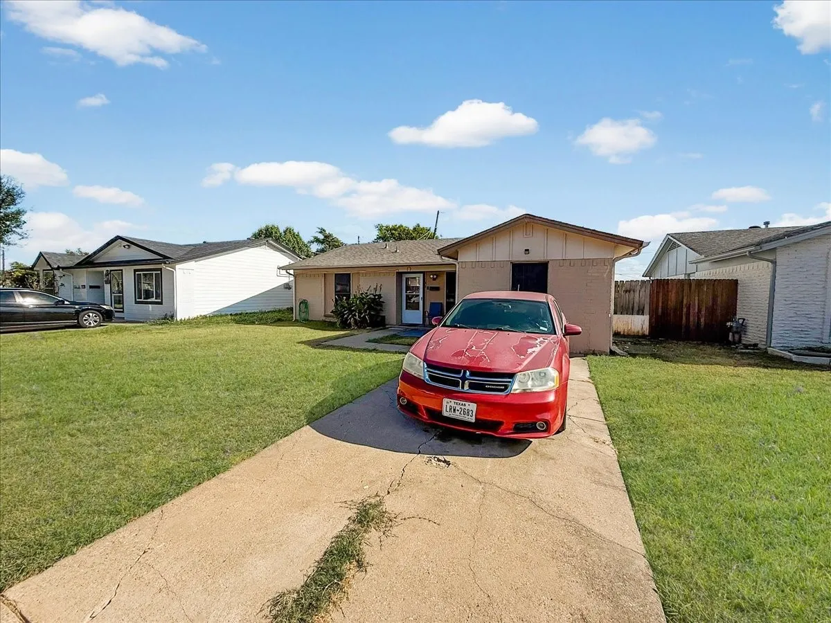 Angled front profile highlighting the front yard lawn, paved parking, and clear blue skies.