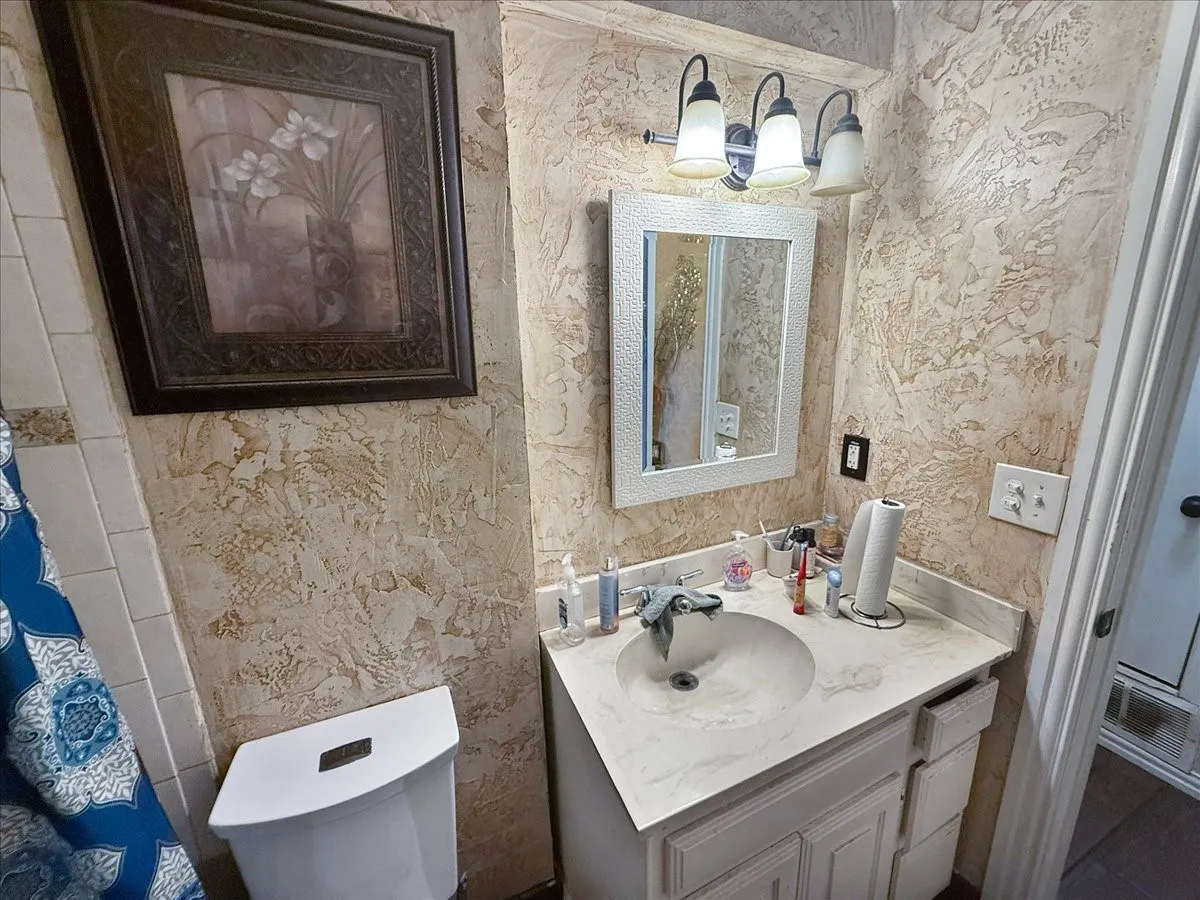 En-suite bathroom vanity featuring stone-look wall tile finishes and modern vanity light fixture.
