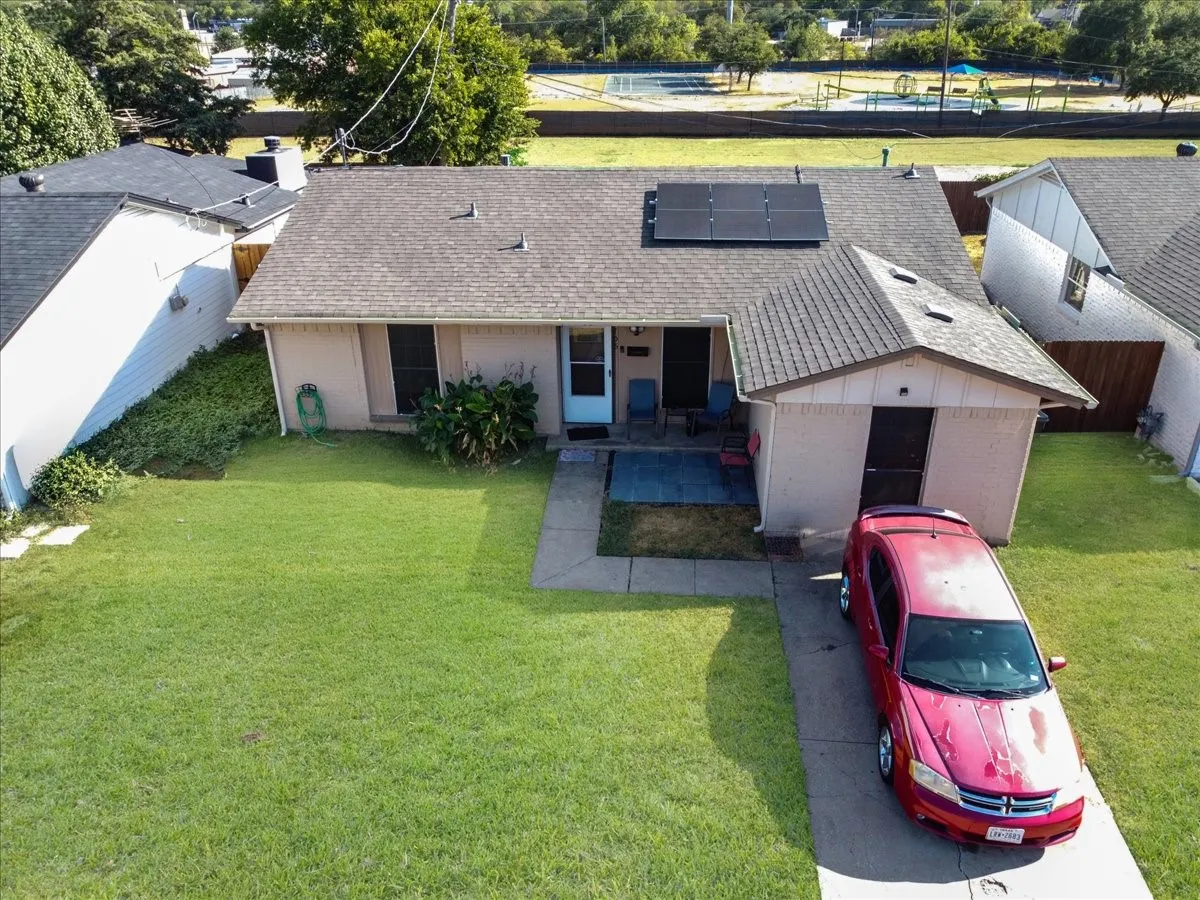 High-angle perspective capturing the home's roofline, solar energy setup, wide yard, and driveway parking.