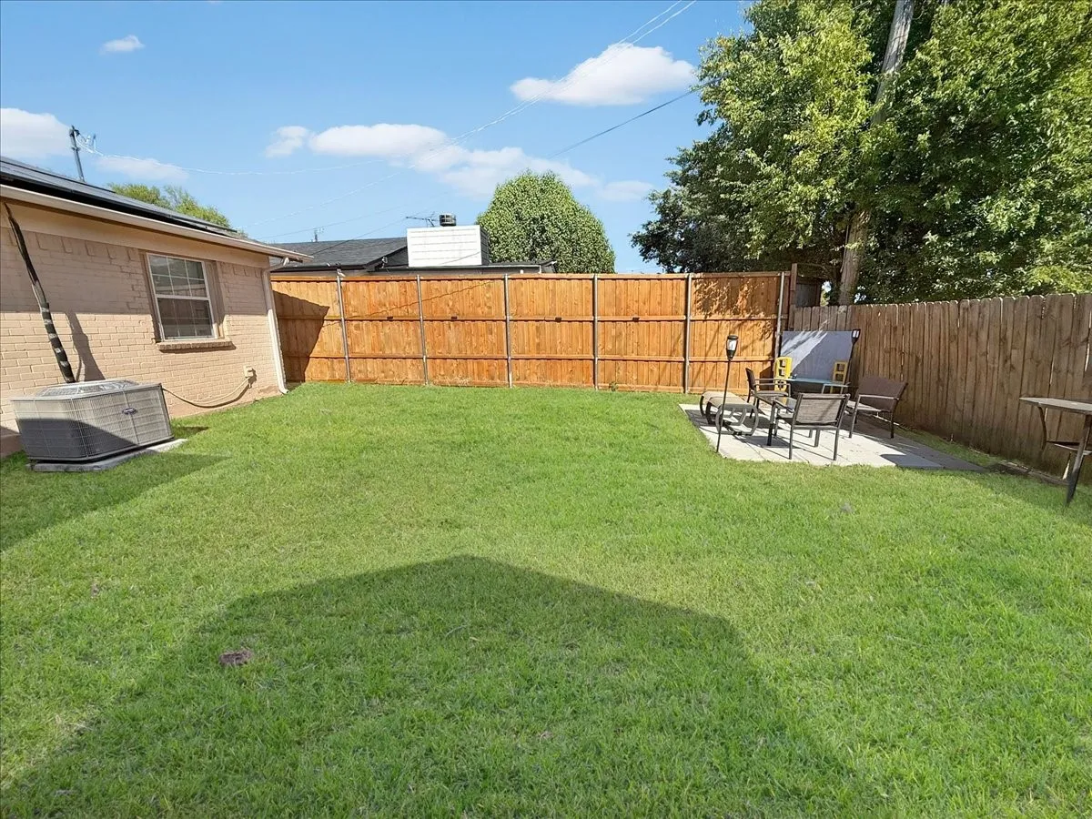 Expansive, fully fenced backyard featuring a lush green lawn, privacy fencing, and shade trees.