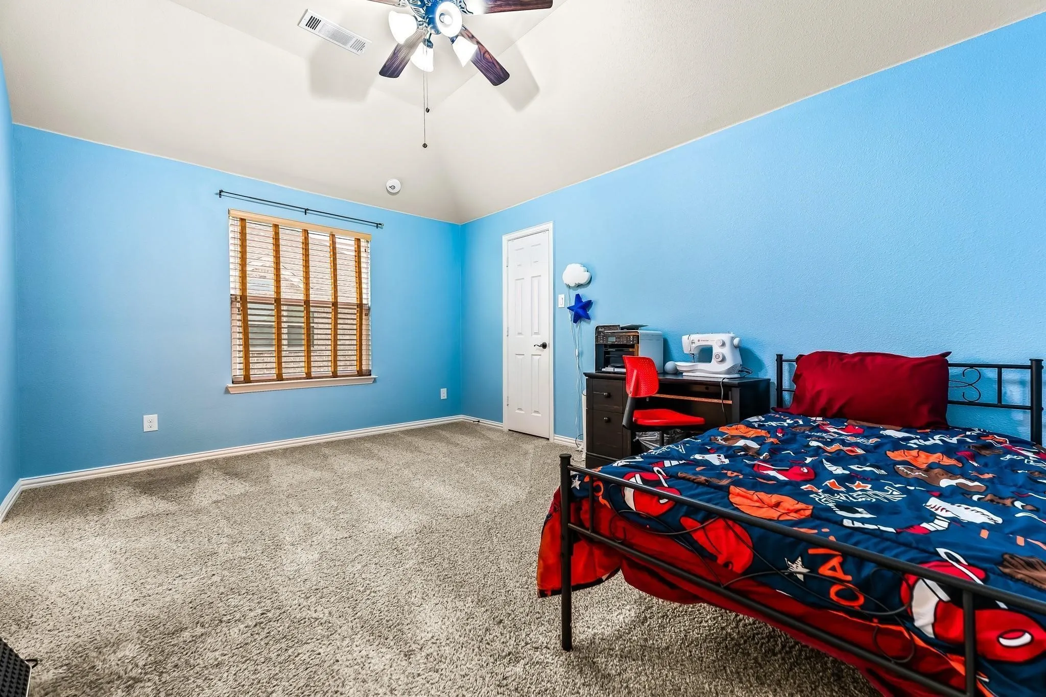 Vaulted ceiling with a ceiling fan, window with horizontal blinds, light-toned carpet flooring, and a white door