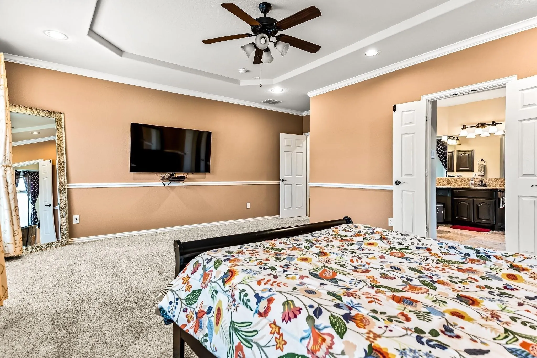 Recessed ceiling, ceiling fan with integrated lighting, wall-mounted television, double doors, and a bathroom vanity with dual sinks
