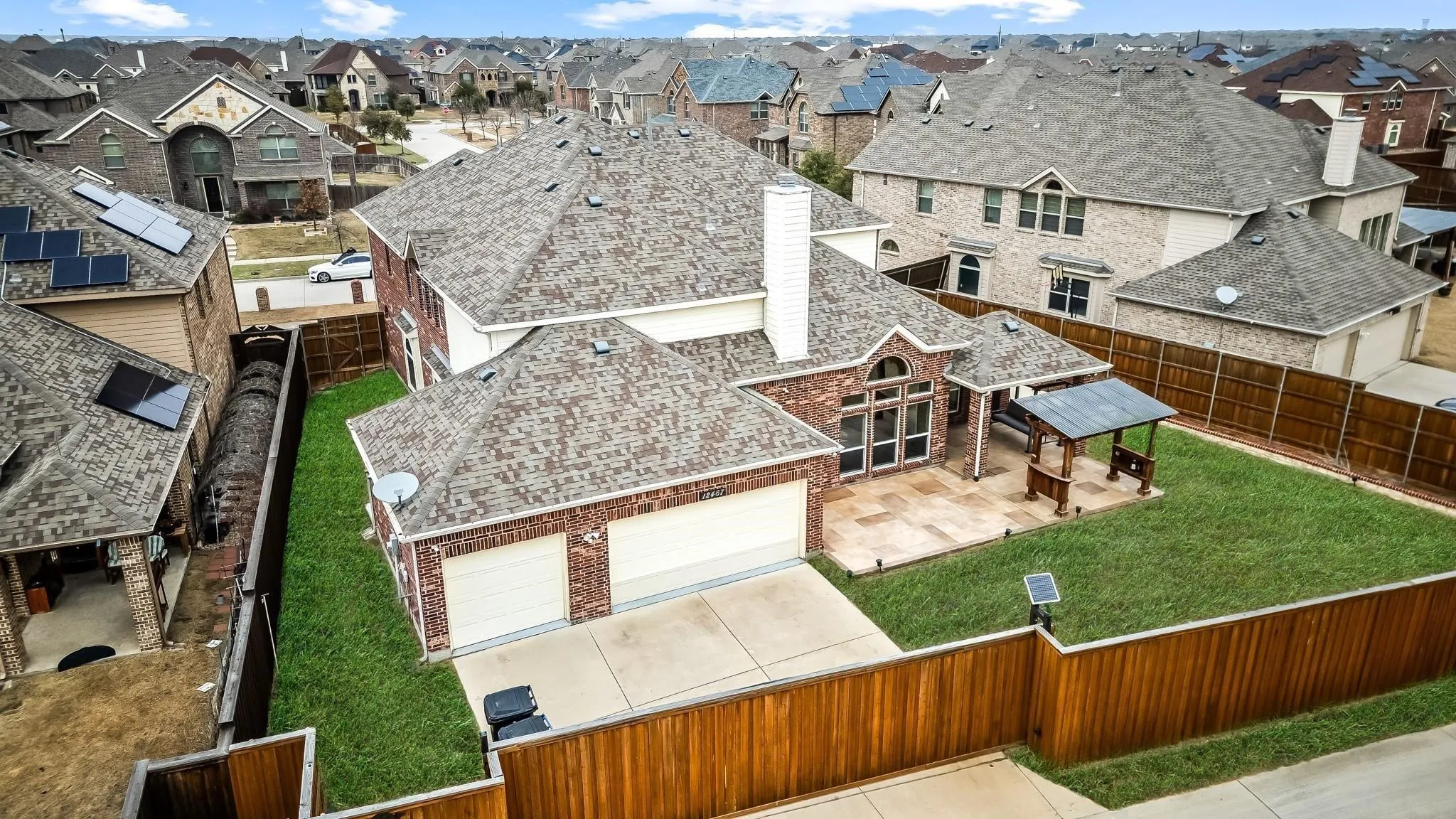 Rear elevation featuring a brick exterior, a two-car garage, an expansive patio, and a covered outdoor structure