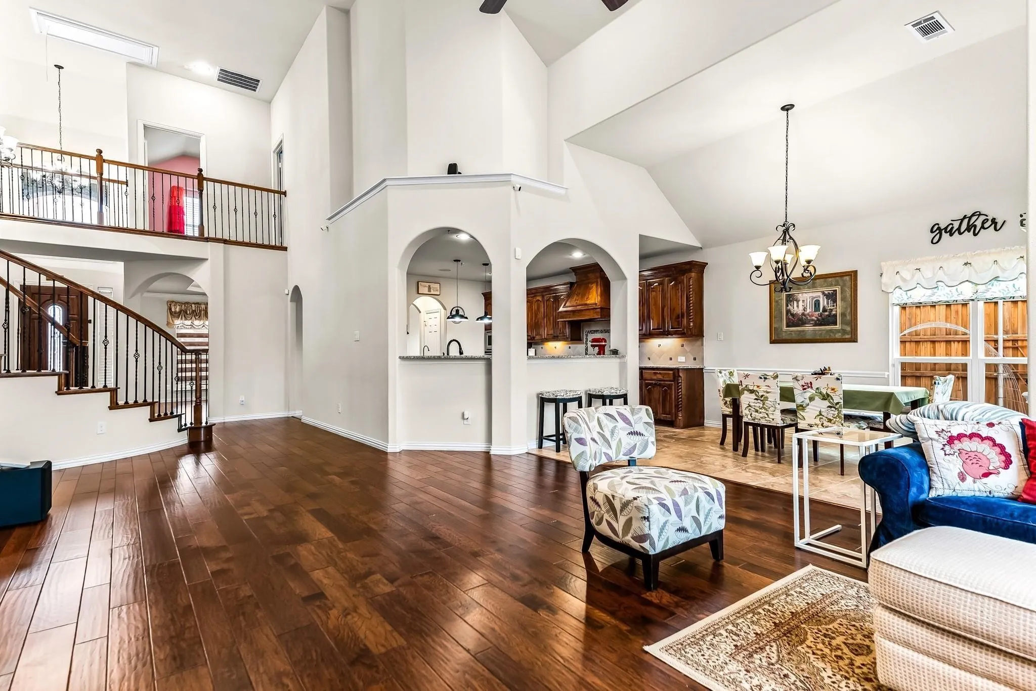 Vaulted ceilings, wood-finish flooring, staircase with wrought iron balusters, arched openings, and recessed lighting