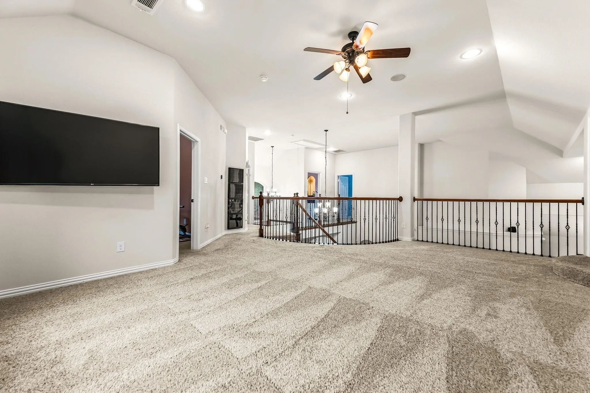 Expansive carpeted loft with vaulted ceiling, recessed lighting, and a ceiling fan