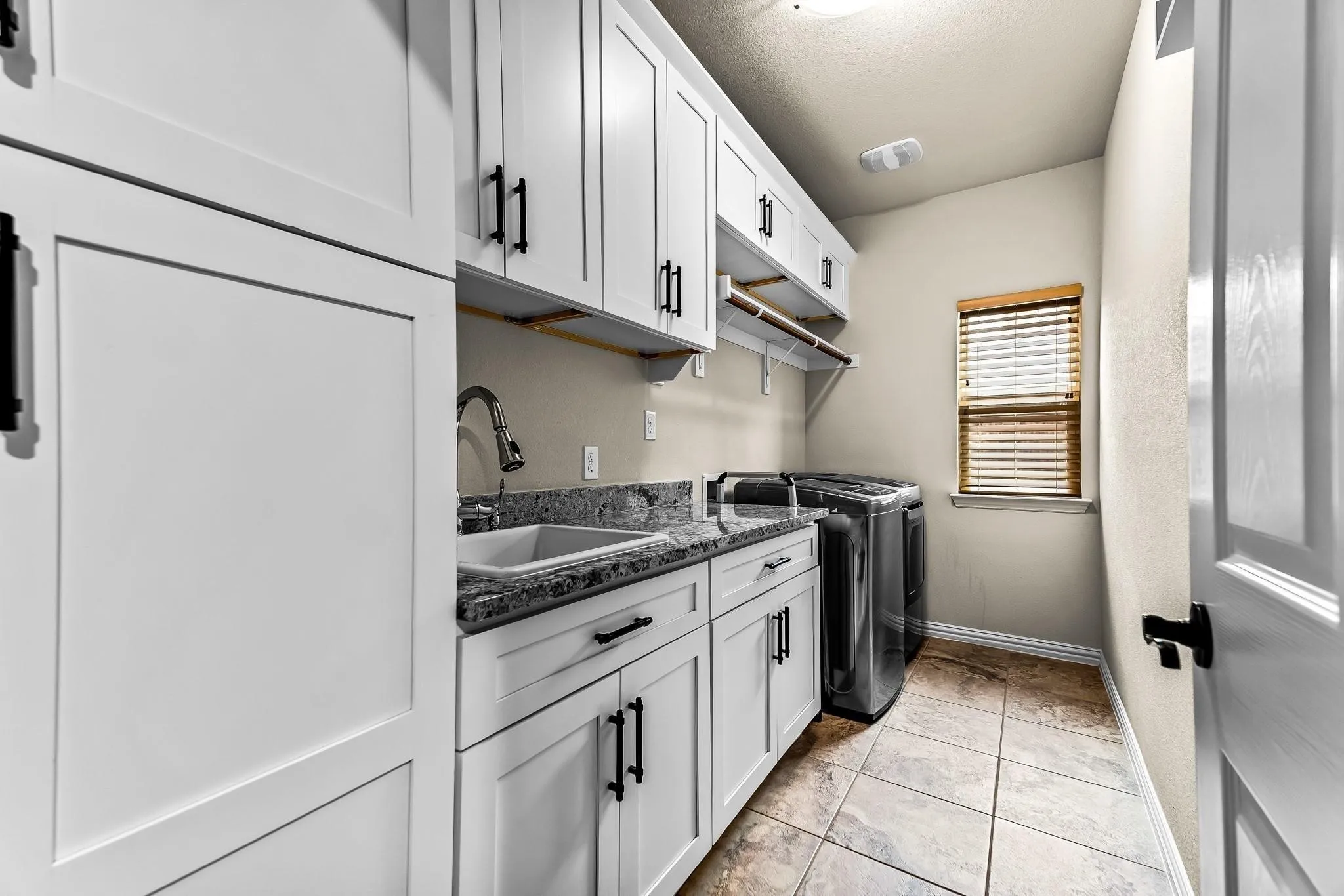 Laundry room featuring extensive white cabinetry, a utility sink, granite-style countertops, and tiled flooring