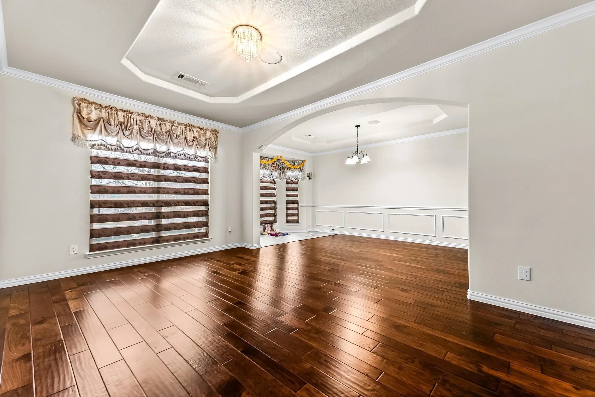 Wood-finish flooring, tray ceiling with a chandelier, crown molding, and wainscoting