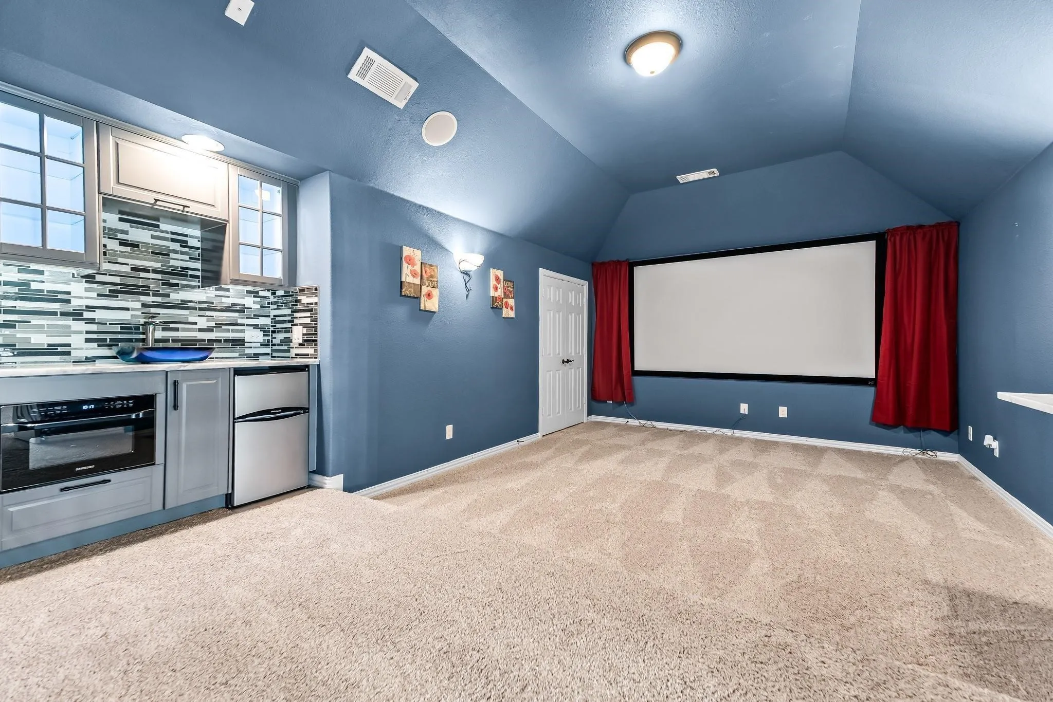 Media room featuring a built-in wet bar with gray cabinetry, a glass tile backsplash, and an integrated refrigerator