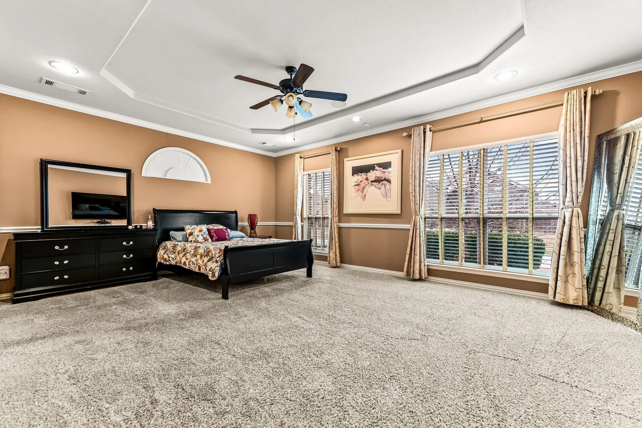 Recessed lighting, ceiling fan, tray ceiling, carpeted flooring, and large windows with blinds