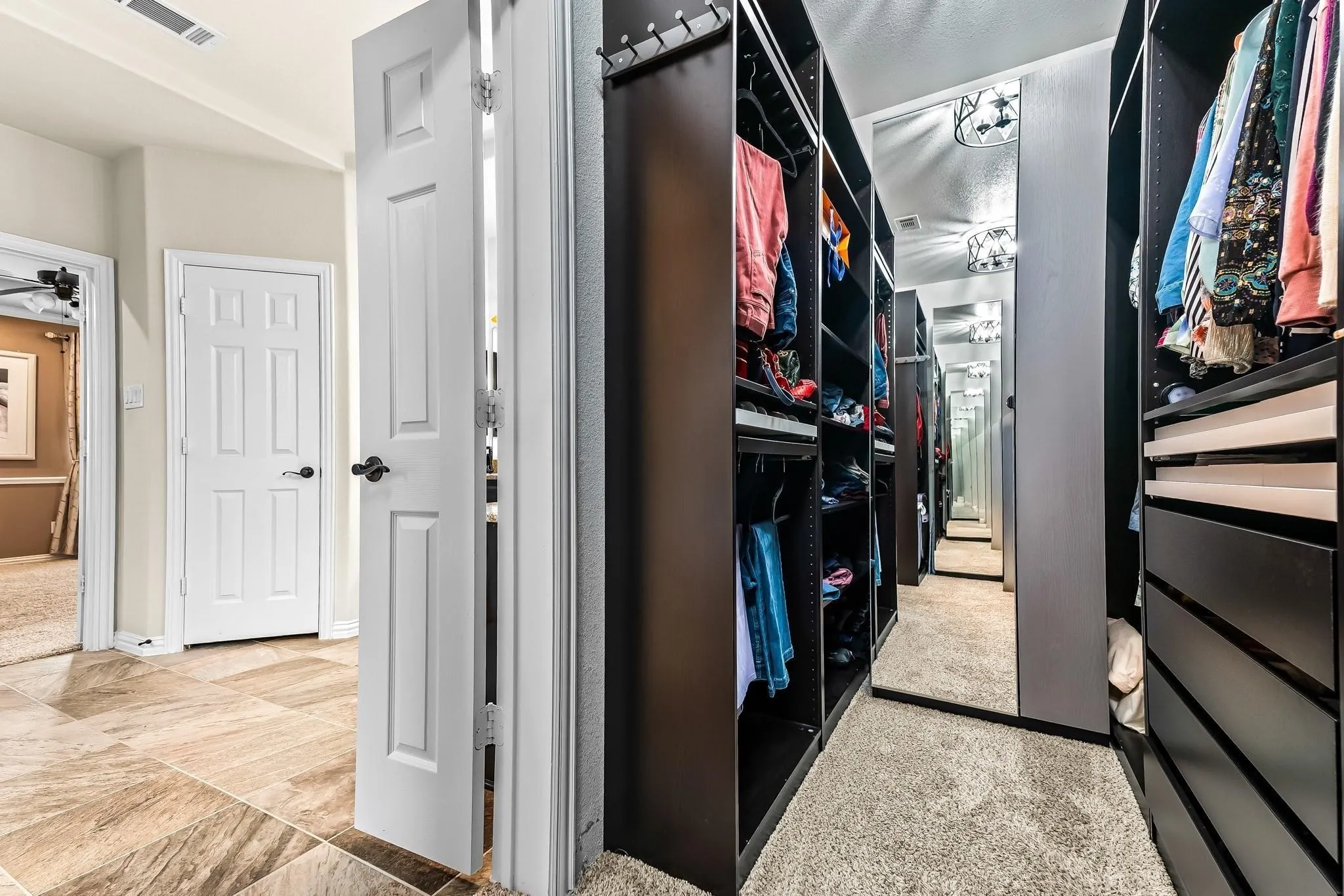 Hallway featuring tile flooring, leading to a custom closet with built-in dark wood cabinetry and carpet flooring