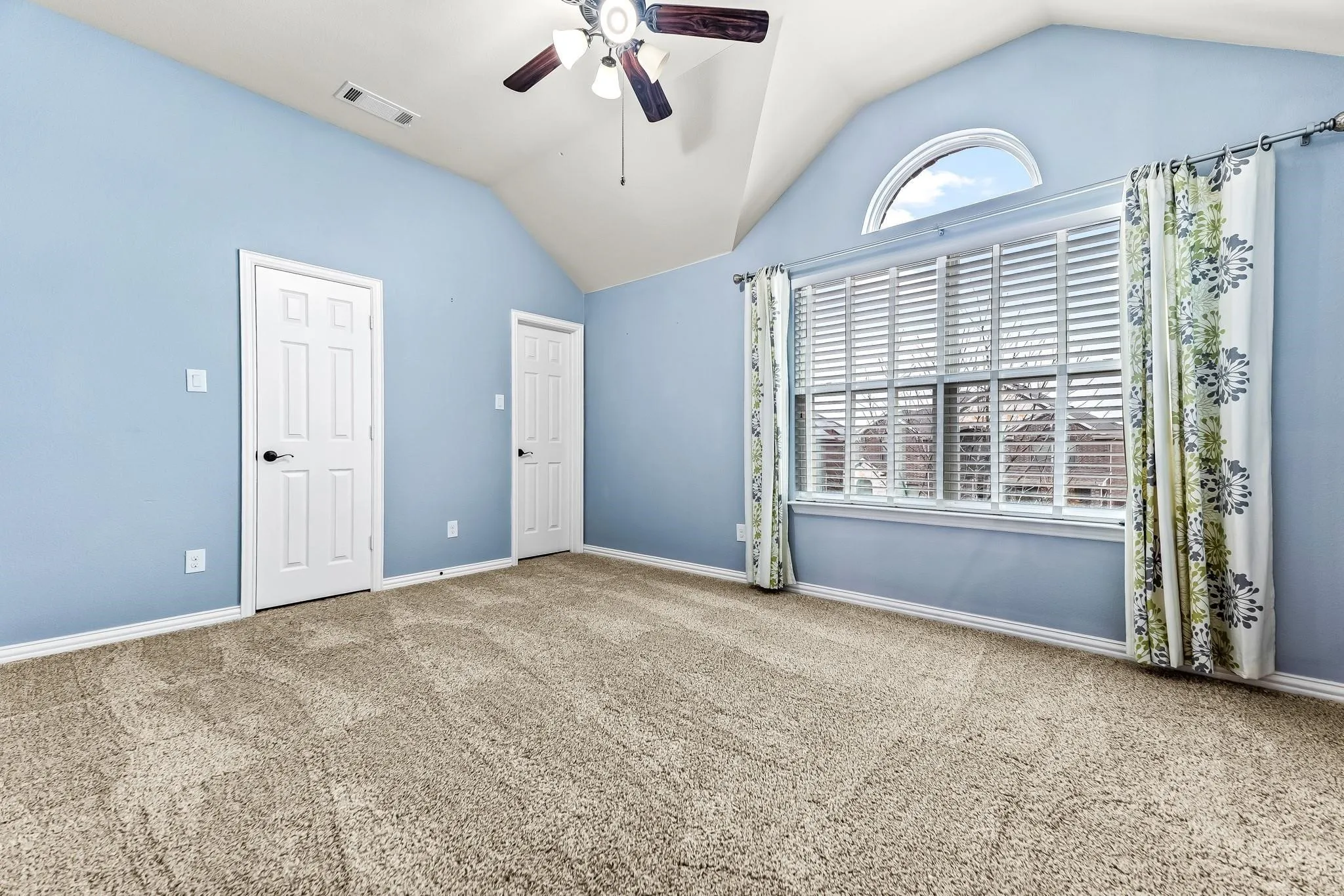 Vaulted ceiling, ceiling fan with light fixture, arched window, six-panel interior doors, and carpeted flooring