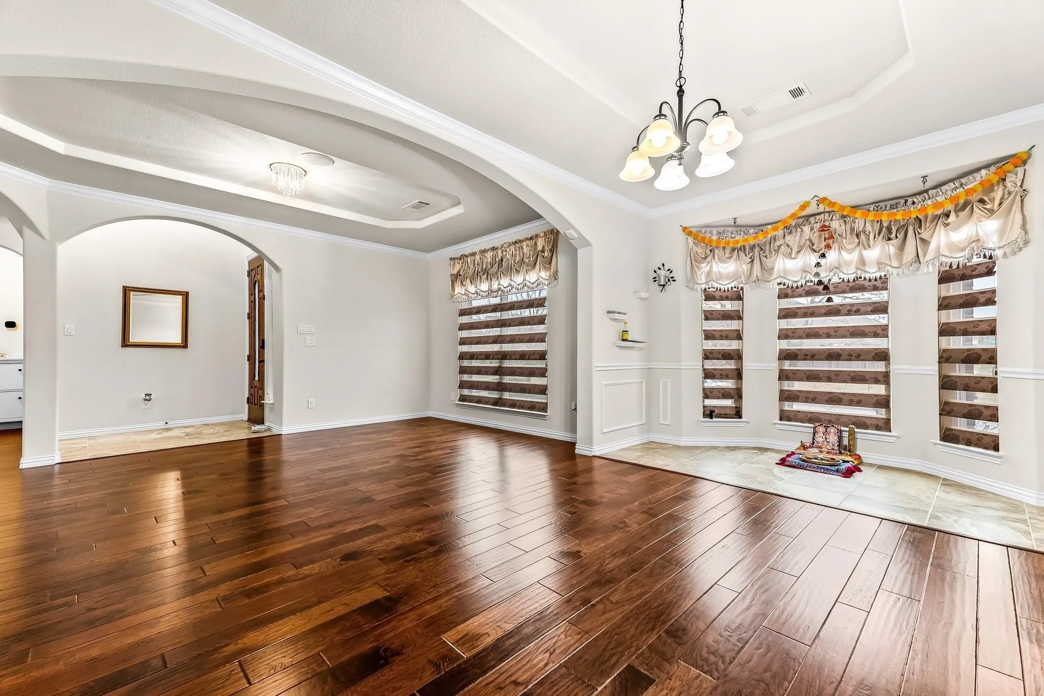 Wood-finish flooring throughout, tray ceiling with recessed lighting, arched doorway, and a chandelier lighting fixture