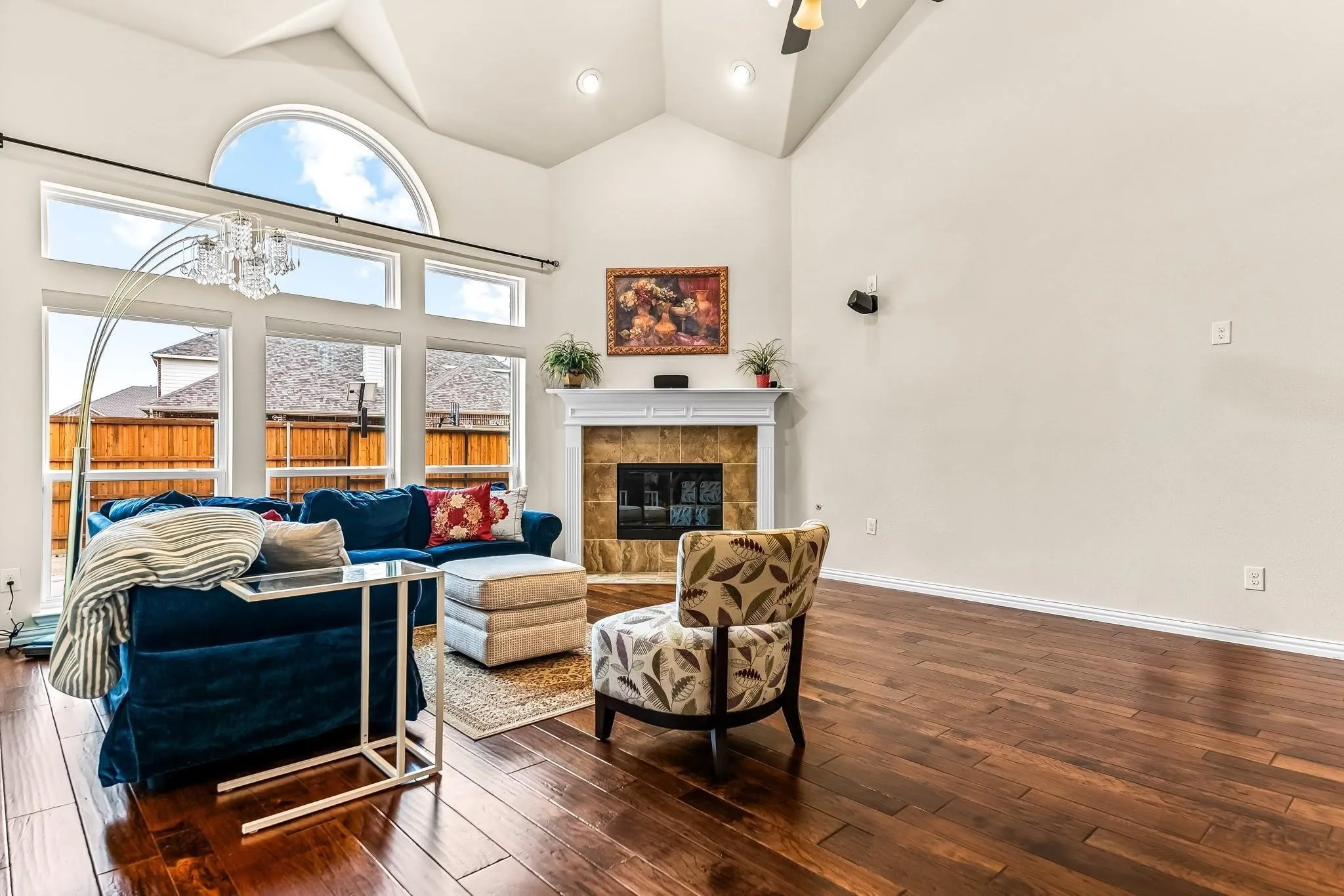Vaulted ceiling, arched transom window, wood-finish flooring, fireplace with tile surround, and mantel