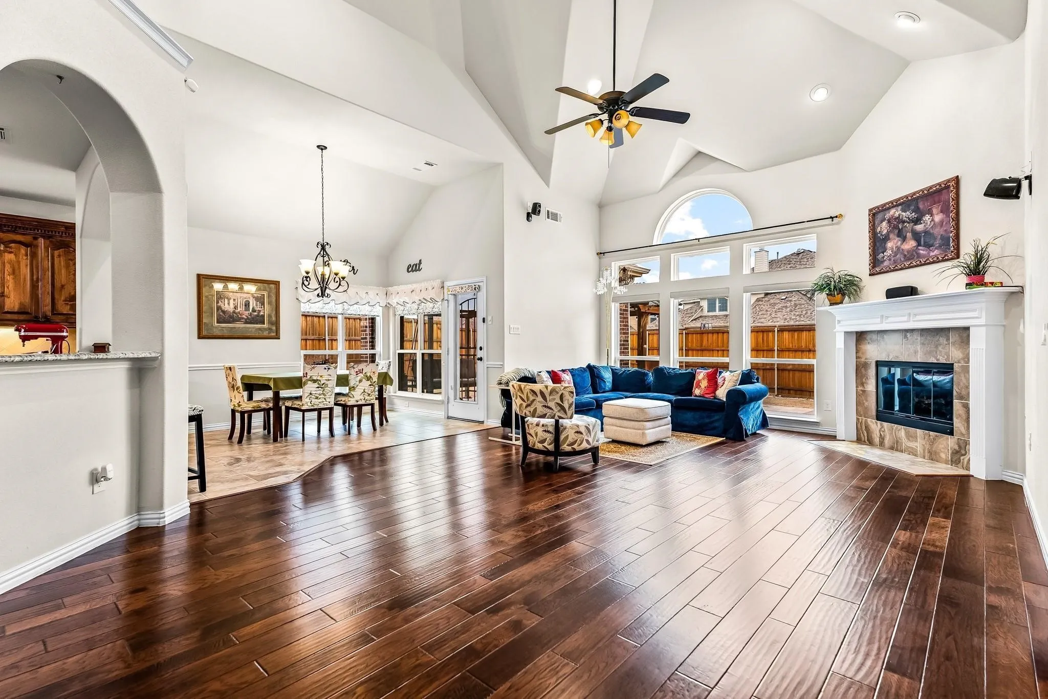 Vaulted ceilings with a ceiling fan, fireplace with a mantel, wood-finish flooring, and expansive windows