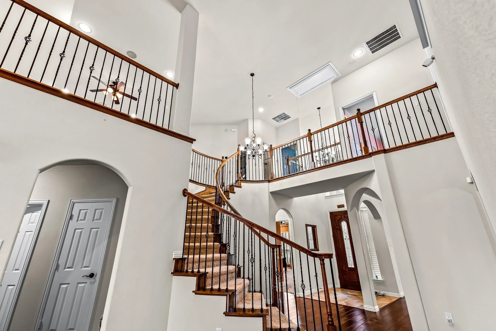 Two-story foyer with a grand curved staircase, wrought iron balusters, wood-finish flooring, and recessed lighting