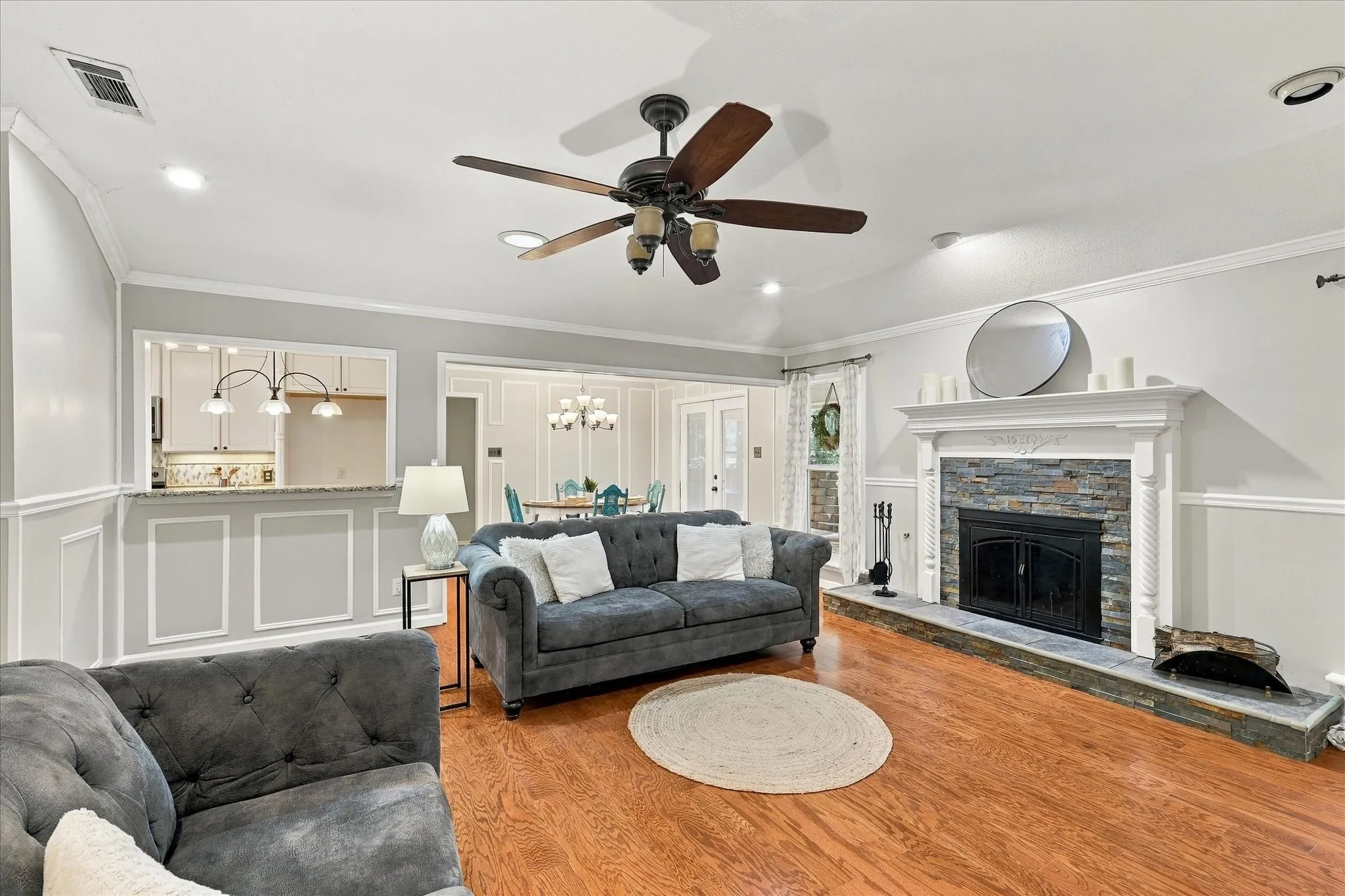Hardwood flooring, crown molding, wainscoting, recessed lighting, and a stone-front fireplace with a decorative mantel