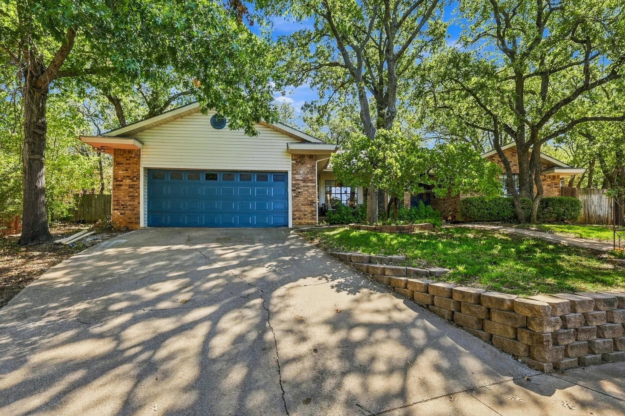 Brick and siding exterior with a blue garage door, concrete driveway, and mature trees