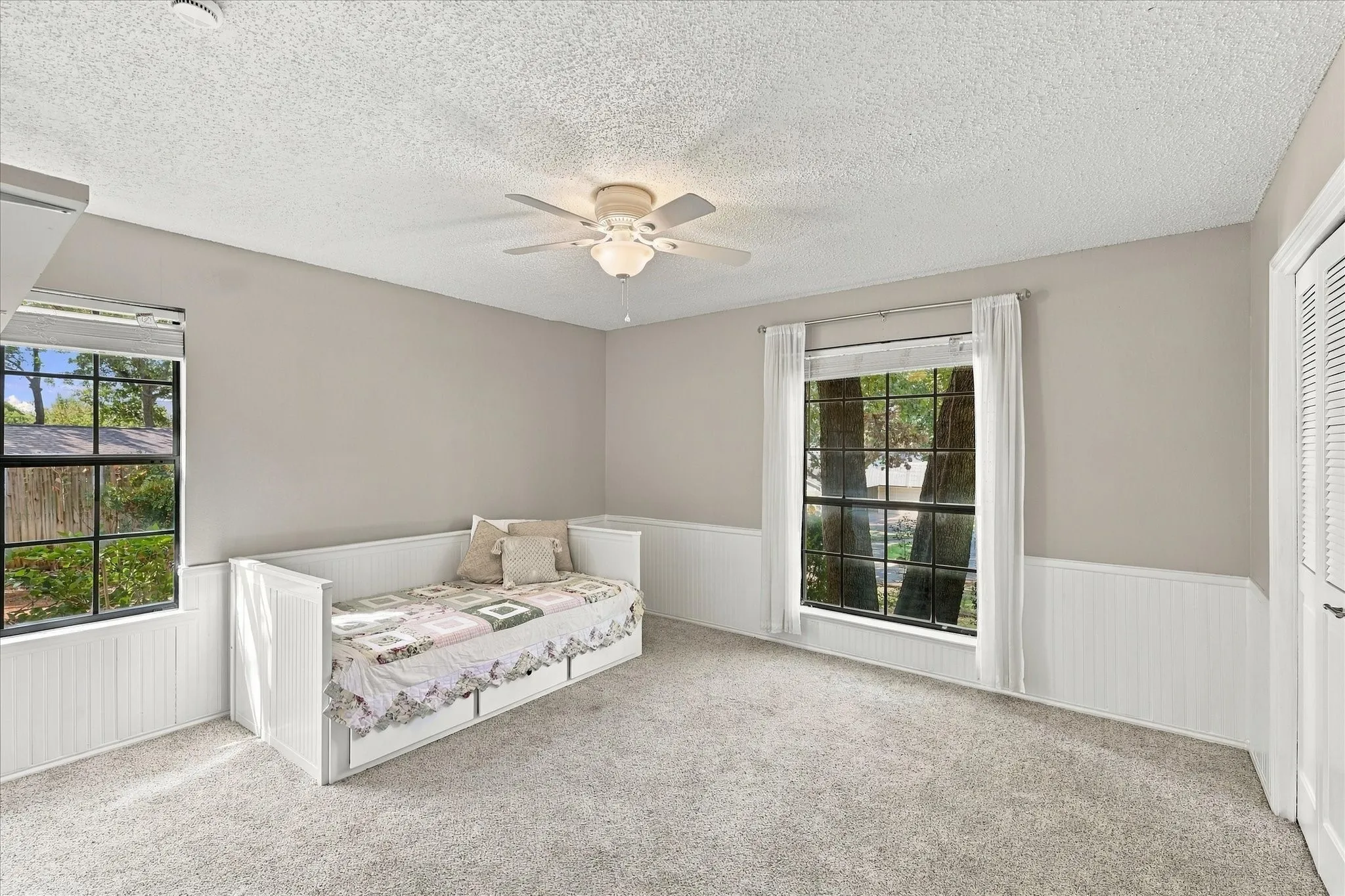 Carpeted flooring with painted walls, white wainscoting, and a ceiling fan with light fixture