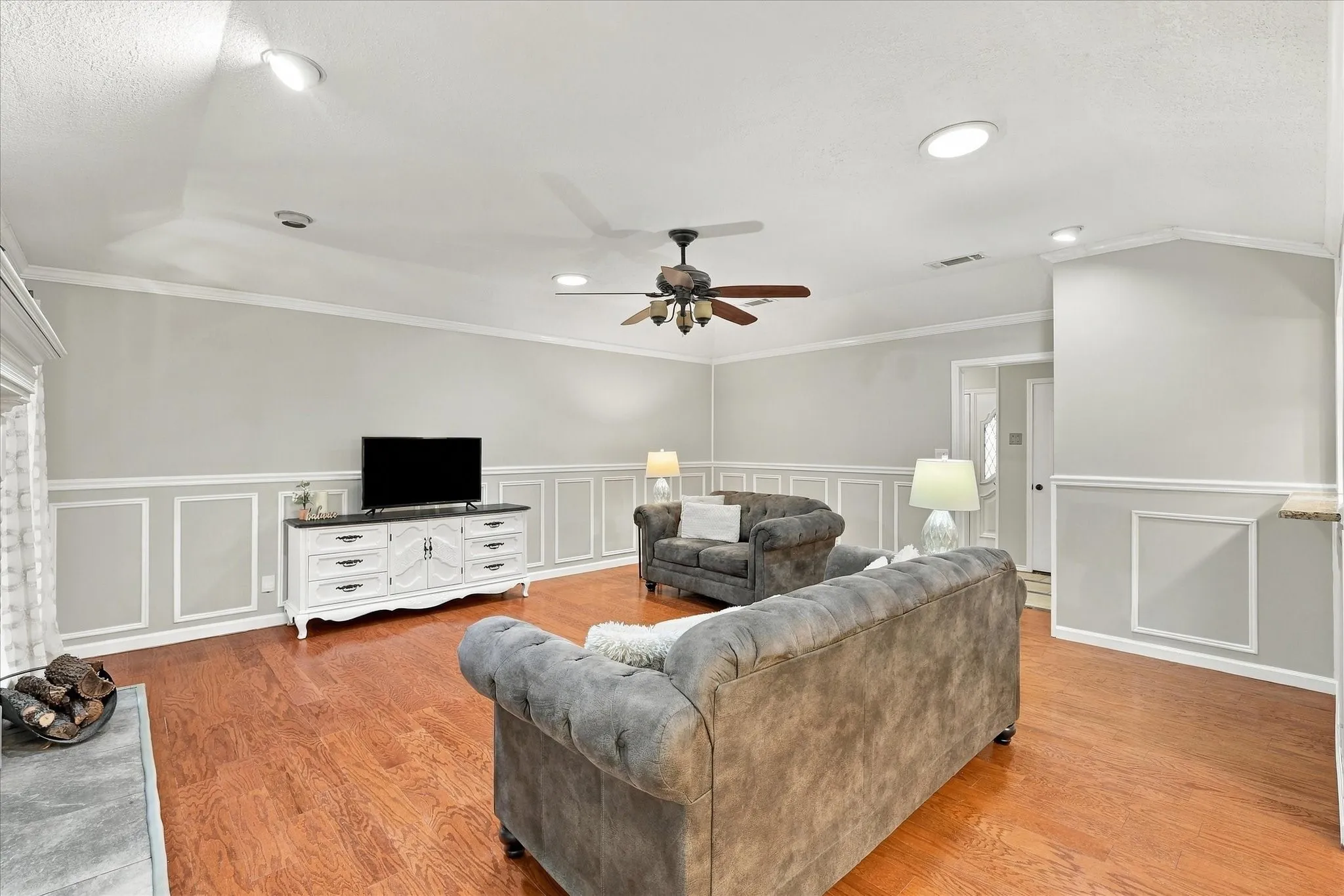 Wood-finish flooring, recessed ceiling lighting, decorative wall paneling, and a ceiling fan with integrated lighting