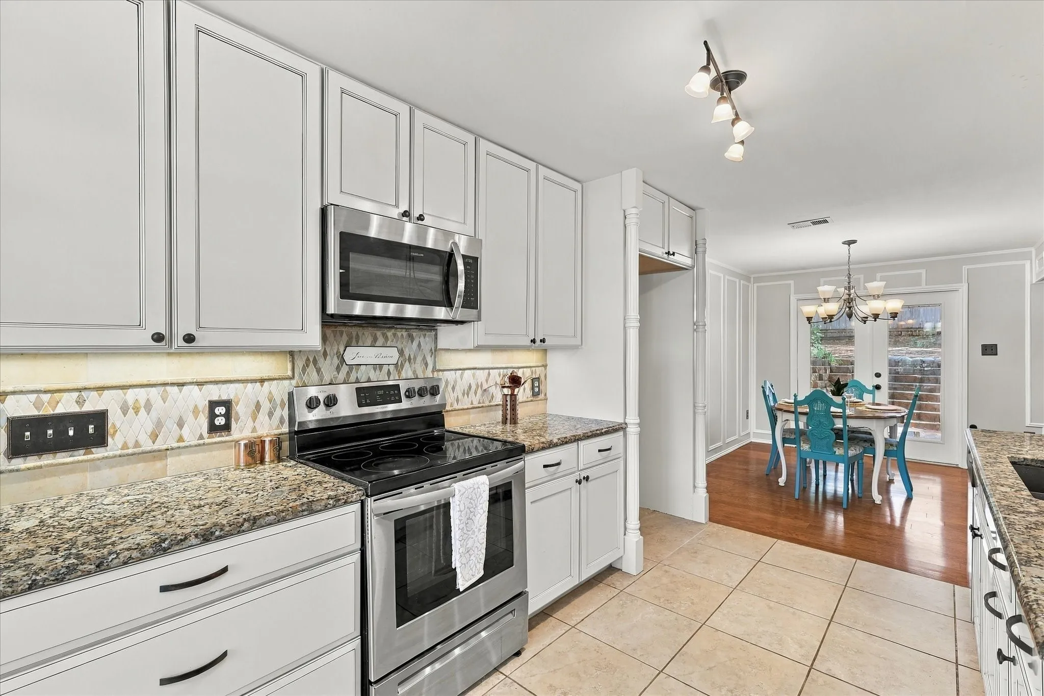 White cabinetry with dark hardware, stainless steel appliances, patterned tile backsplash, granite countertops, and tile flooring