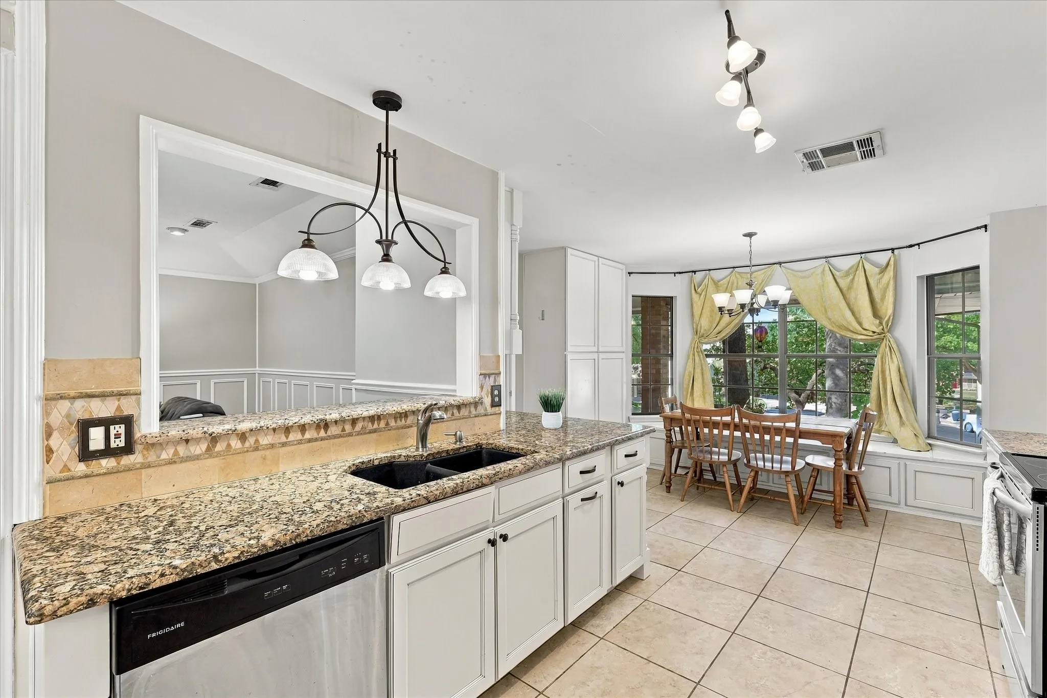 Kitchen featuring granite countertops, white cabinetry, a built-in dishwasher, tile flooring, and an integrated dining area with a bay window and built-in bench seating