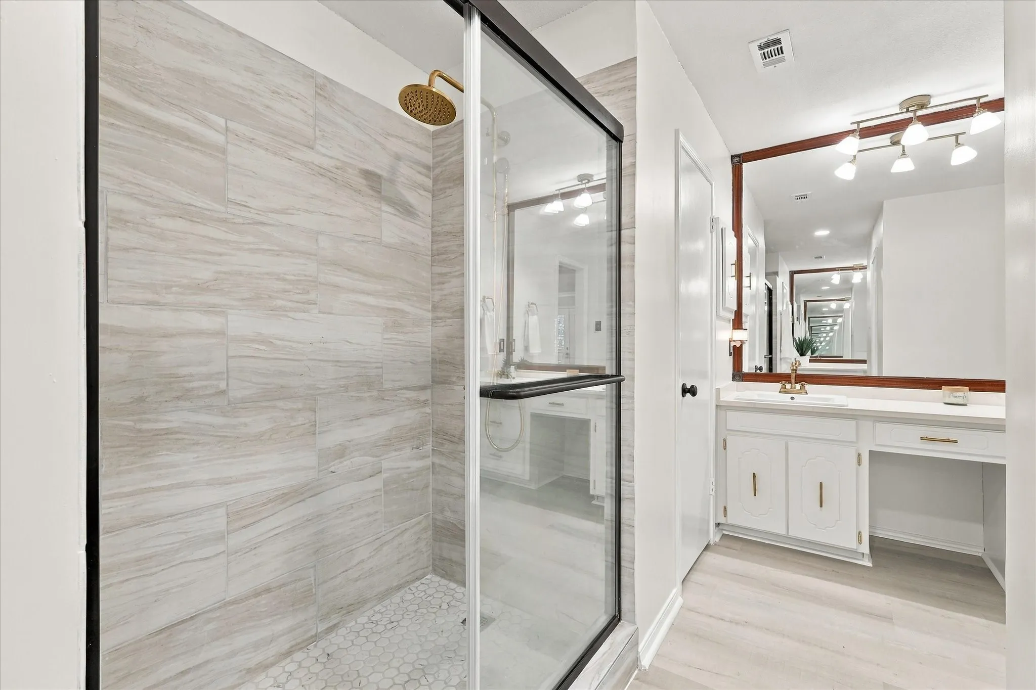 Glass-enclosed shower with a gold-tone rainfall showerhead and light-toned, horizontally-laid wall tile