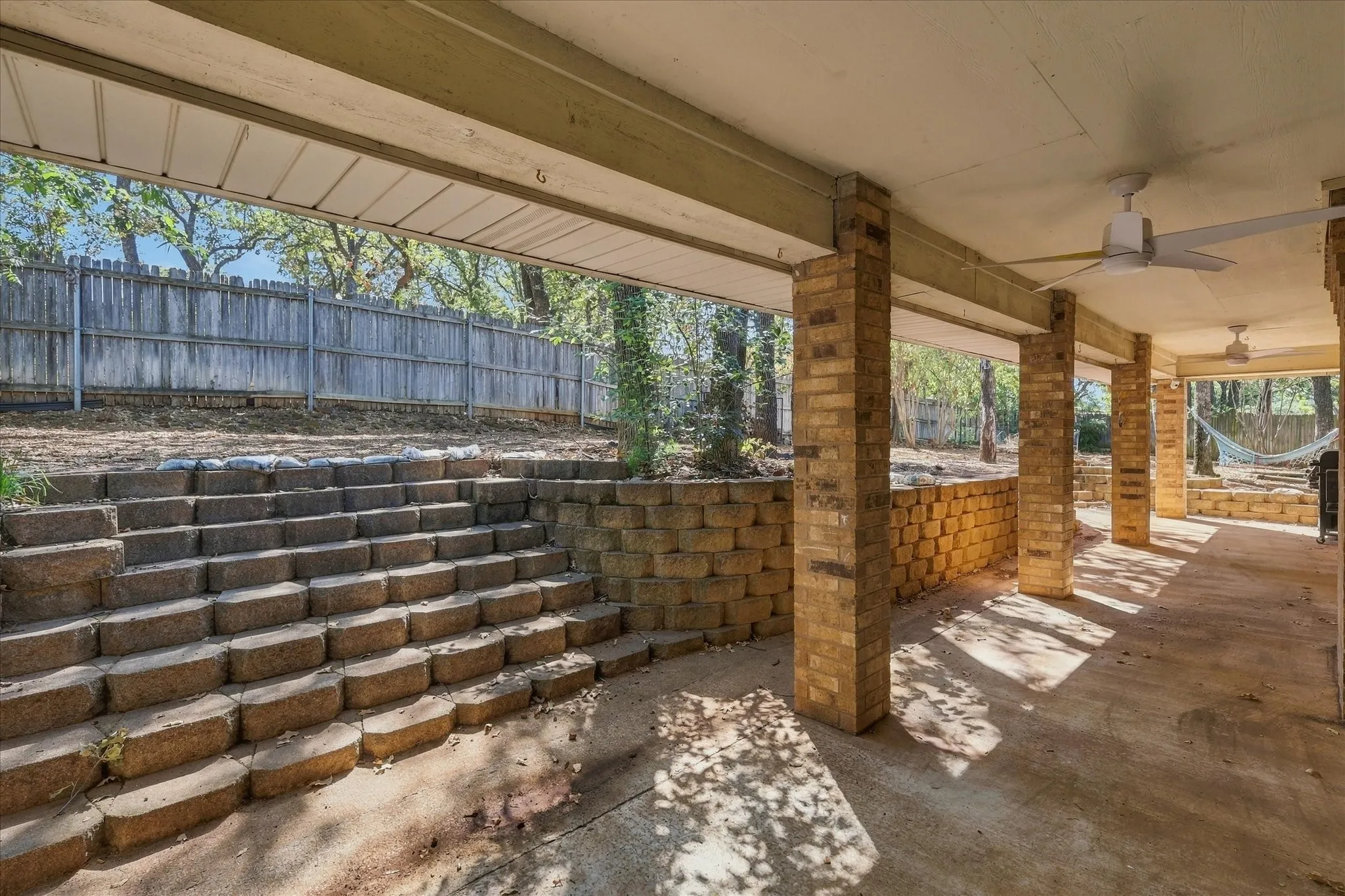 Expansive covered patio featuring concrete flooring, brick support columns, and ceiling fans