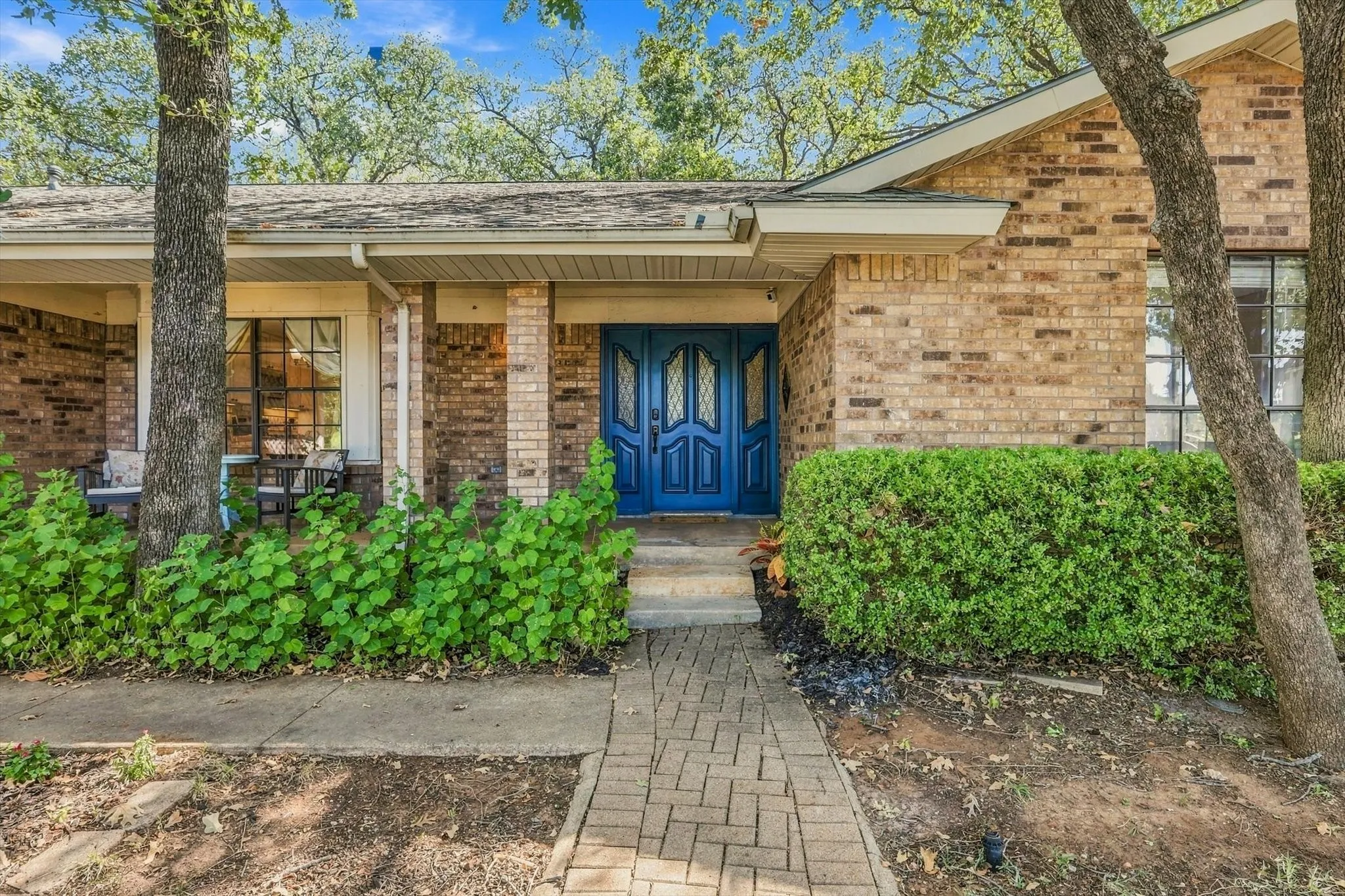 Brick exterior with a distinctive blue double entry door, covered porch, large front windows, and mature trees