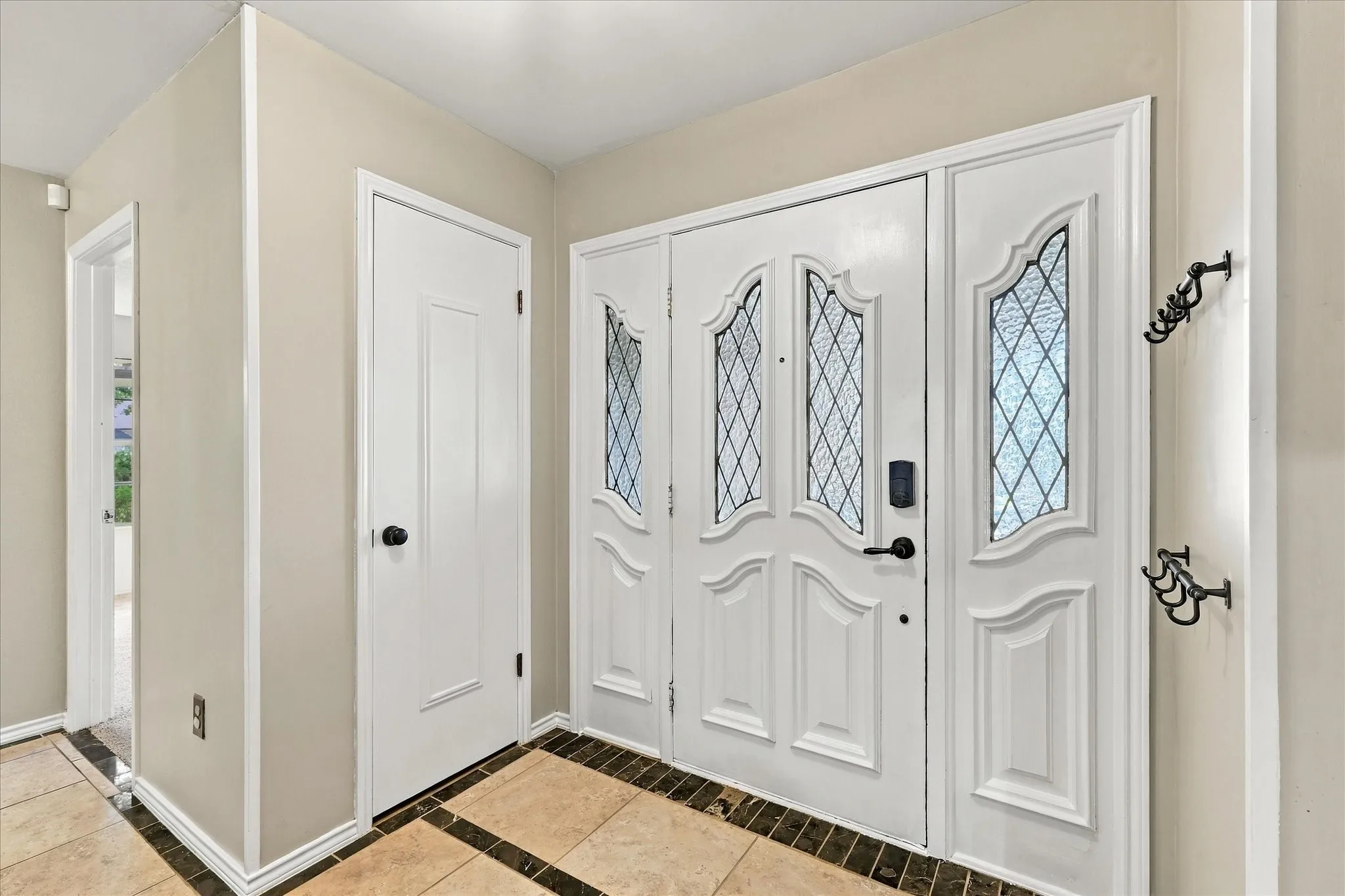 Entryway featuring a decorative main door with frosted glass inserts, a white paneled door, and a tiled flooring with contrasting border