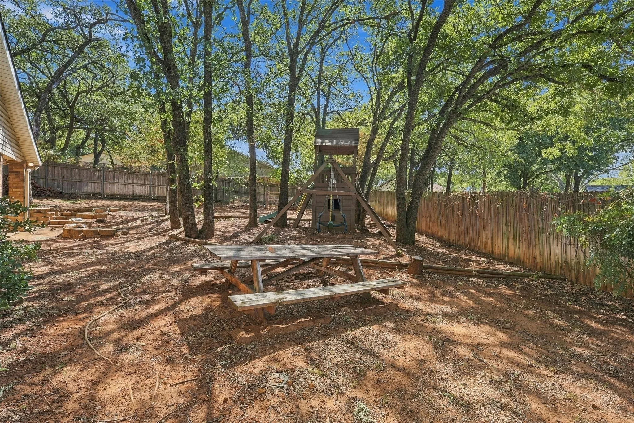 Expansive backyard featuring mature trees, a privacy fence, stone steps, and a built-in play structure