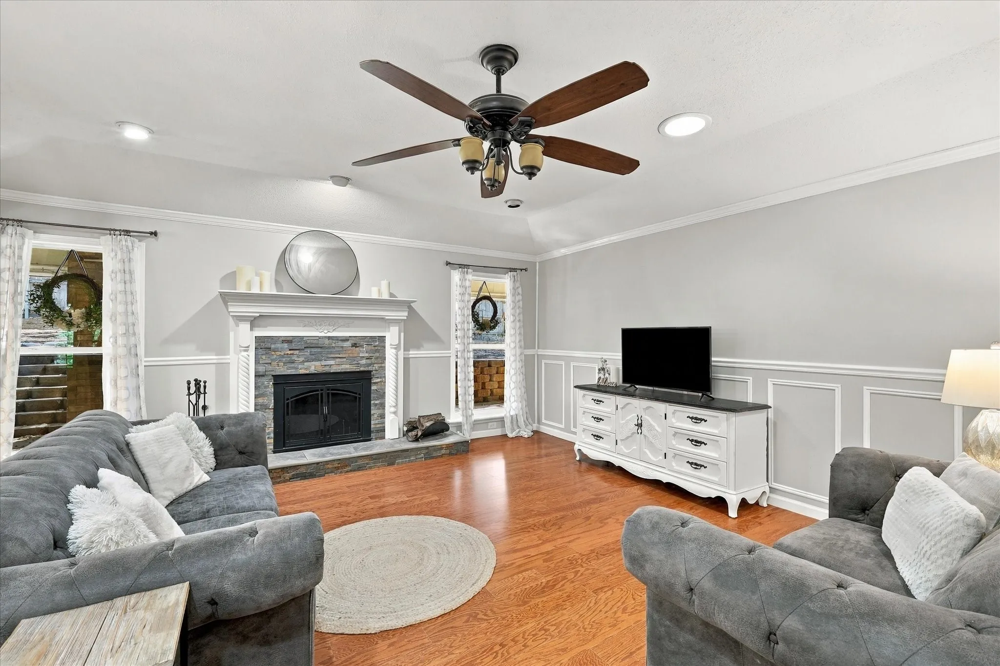 Living space featuring wood-finish flooring, a stone-clad fireplace with a classic mantel, recessed lighting, and a ceiling fan